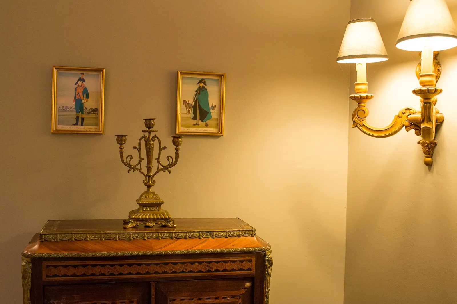 Inlaid chest, gilt candelabra, a lit wall lamp and two prints of soldiers, La Folie Saint Julien