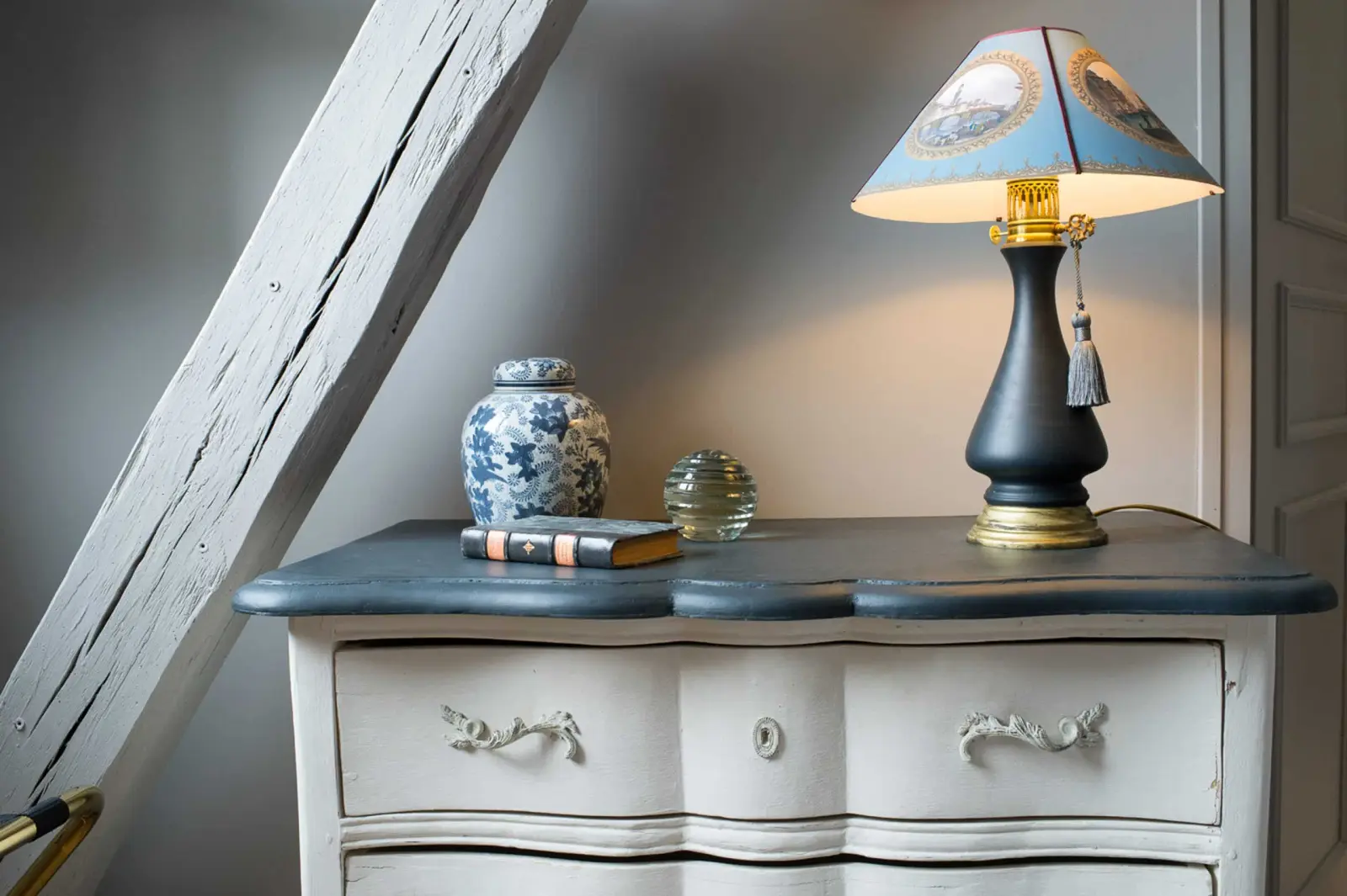 Curved white and grey chest, black-based lamp, blue porcelain jar and a beam, La Folie Saint Julien