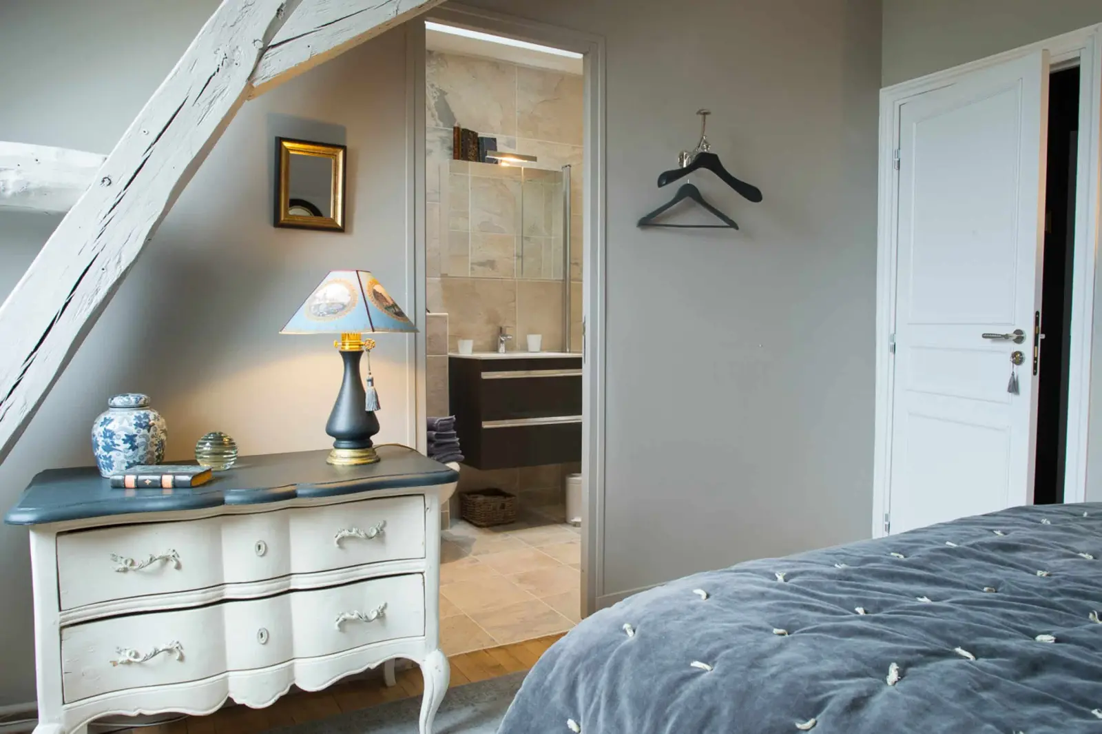 White chest with a grey top, a lamp and a door open onto the bathroom, La Folie Saint Julien