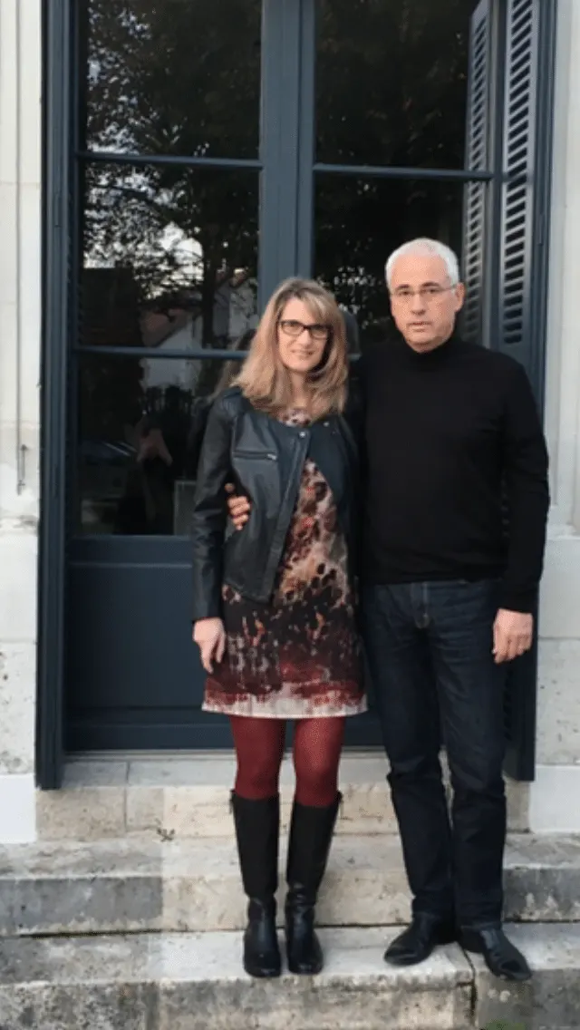 Couple standing in front of a French window with grey shutters, on stone steps, La Folie Saint Julien