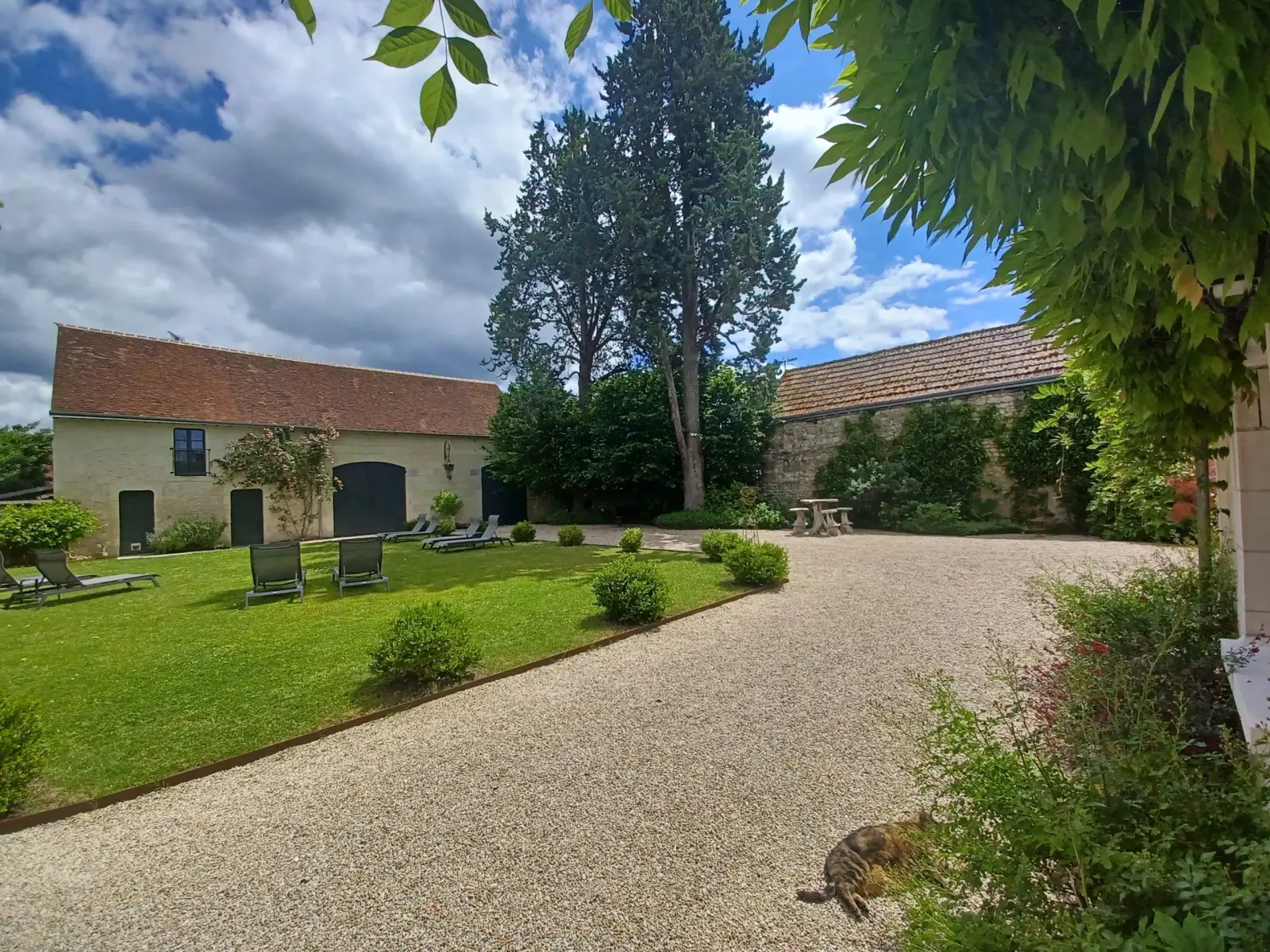 Gravel courtyard lined with stone outbuildings, a lawn and a sleeping cat, La Folie Saint Julien