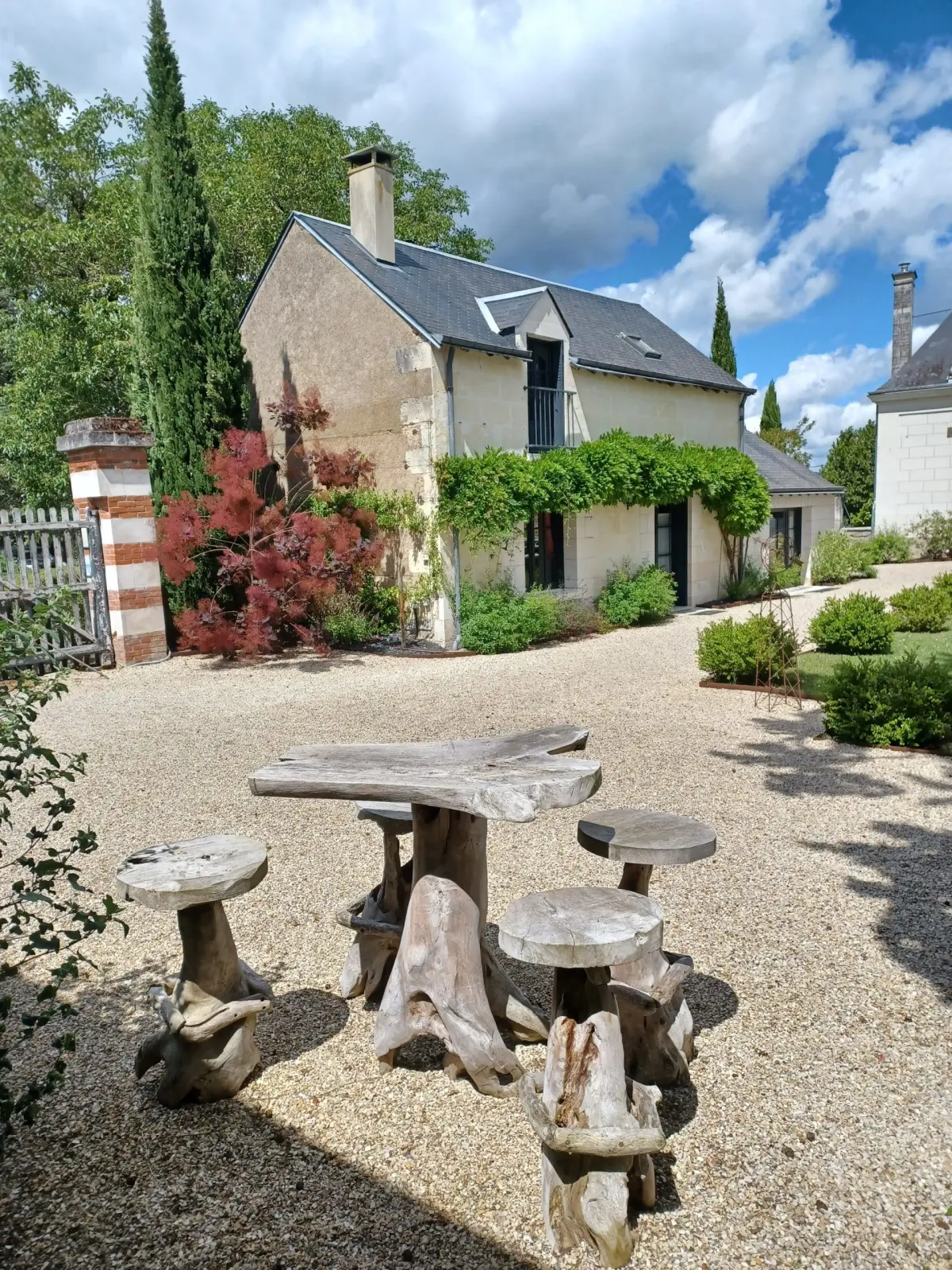 Rough-hewn wooden table and stools on the gravel courtyard before a stone house, La Folie Saint Julien