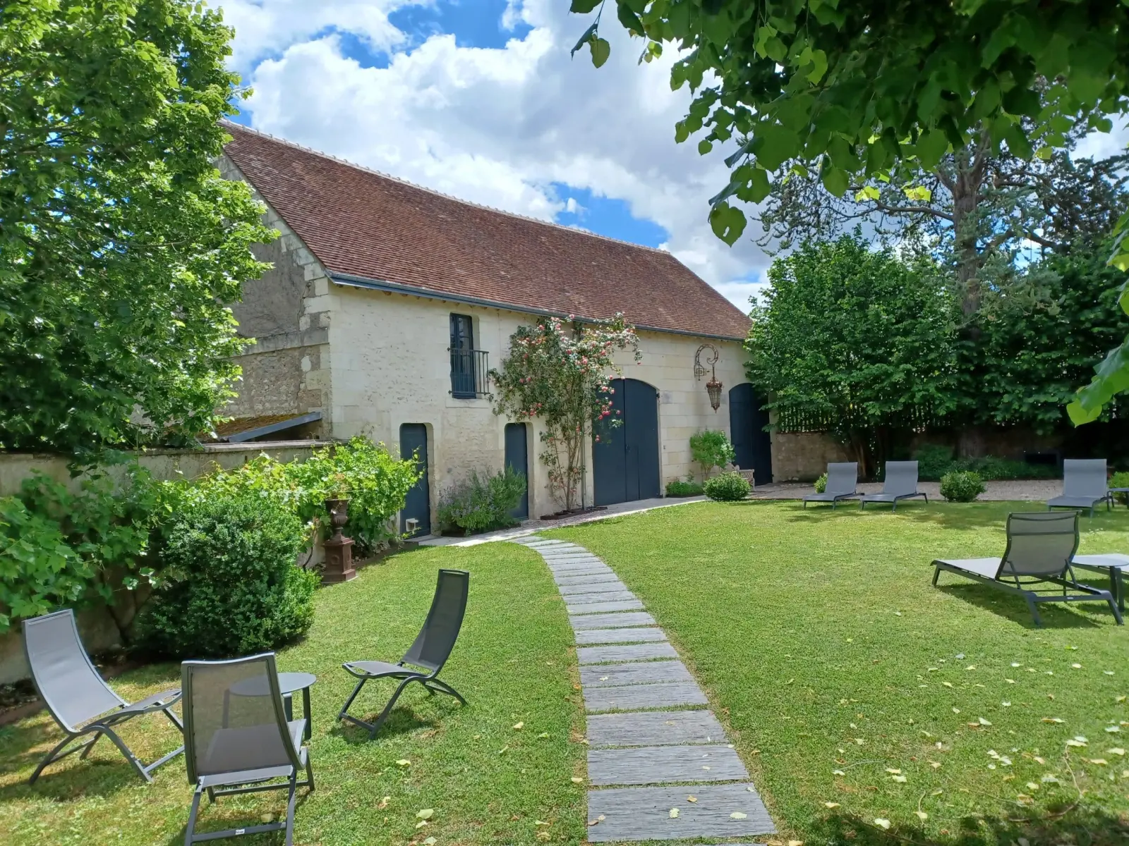 Stone outbuilding with a tiled roof, lawn with loungers and a paved path, La Folie Saint Julien