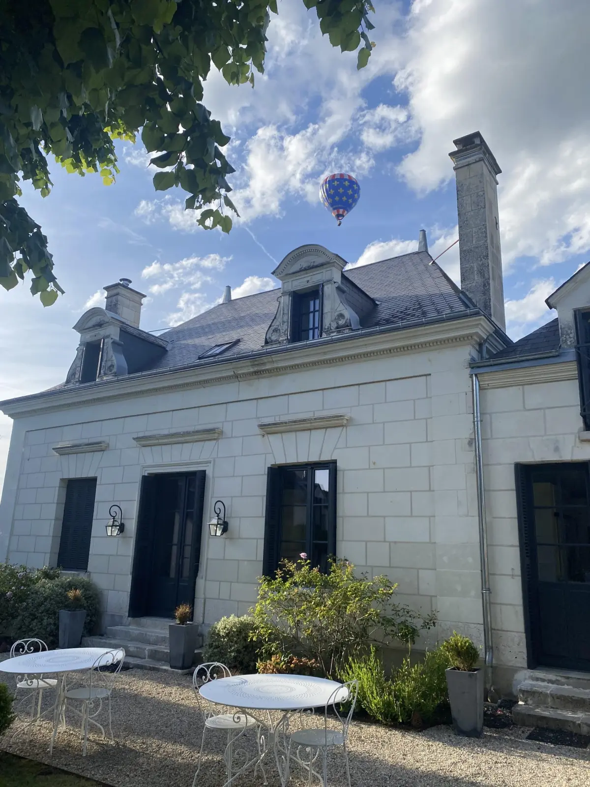 Tufa stone facade with dormer windows, white garden tables and a hot-air balloon in the sky, La Folie Saint Julien