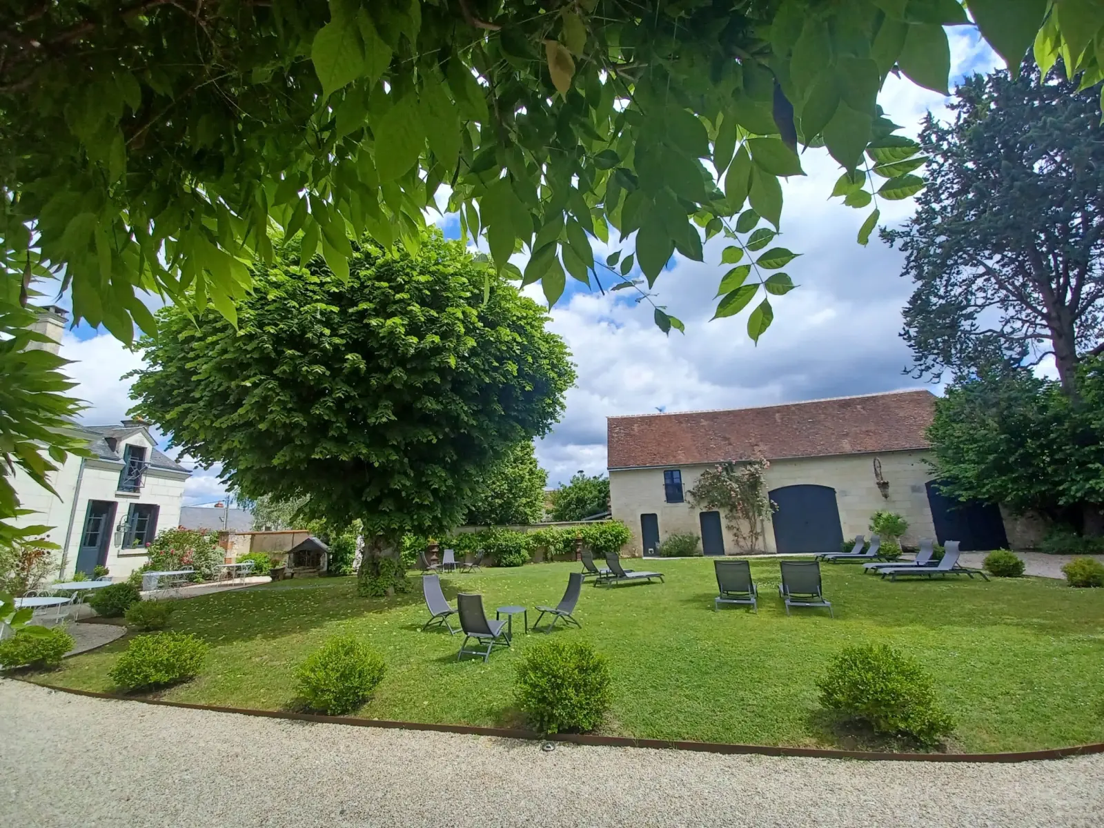 Large garden with a lawn, trees and loungers in front of a stone outbuilding, La Folie Saint Julien