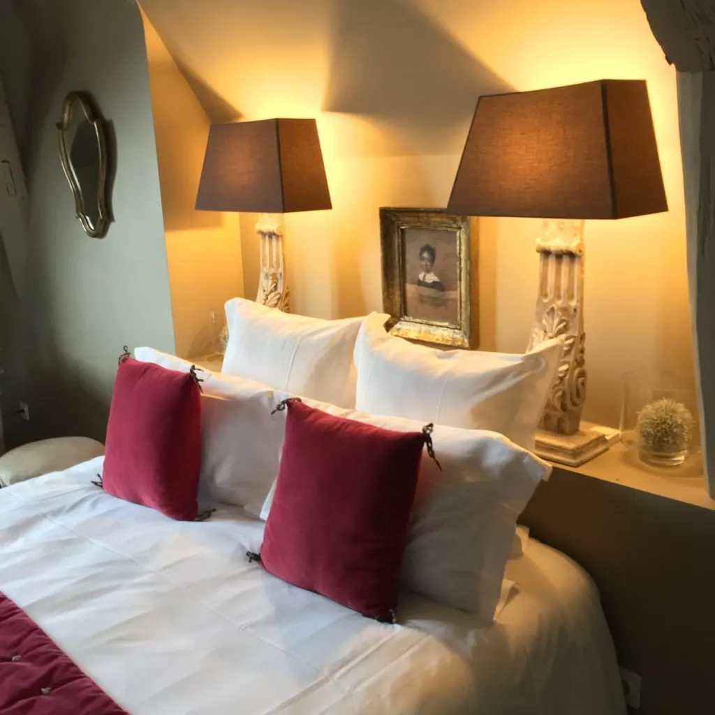 White bed with raspberry cushions, carved-base lamps and a framed old portrait, La Folie Saint Julien