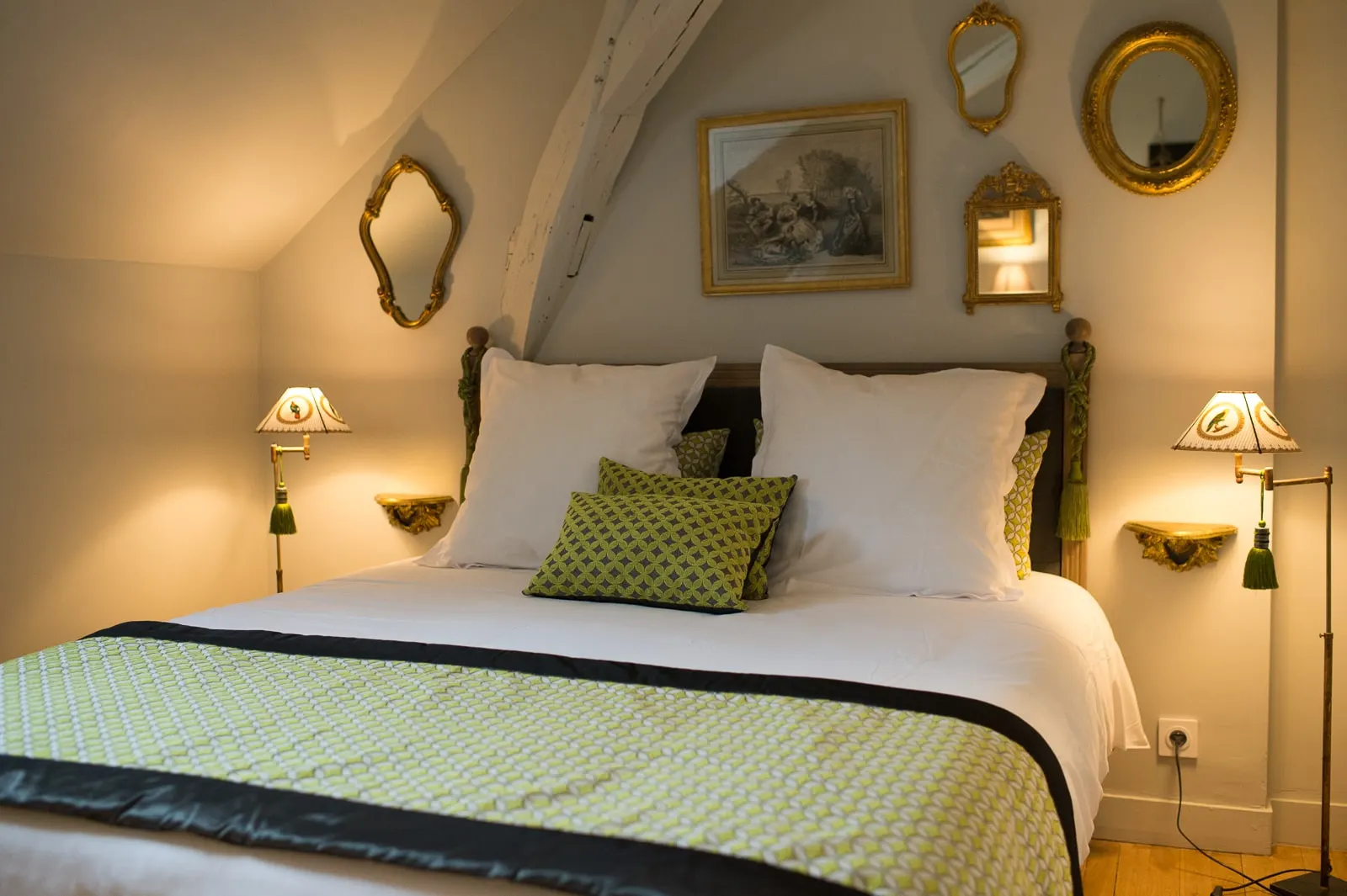 Bedroom under the beams with a white bed, green cushions, gilt mirrors and reading lamps, La Folie Saint Julien