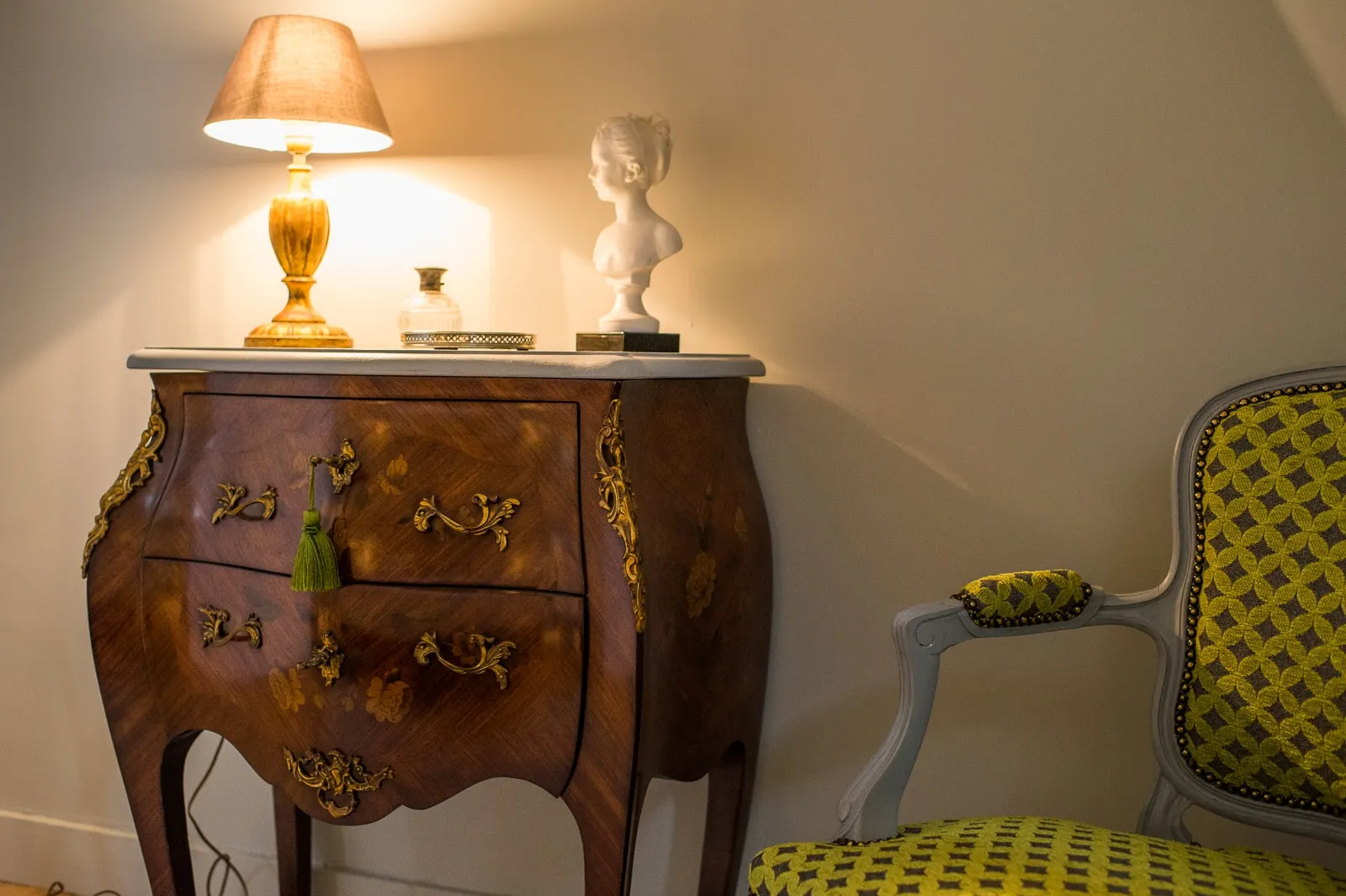 Curved marquetry chest, a lit lamp, a white bust and a green armchair, La Folie Saint Julien