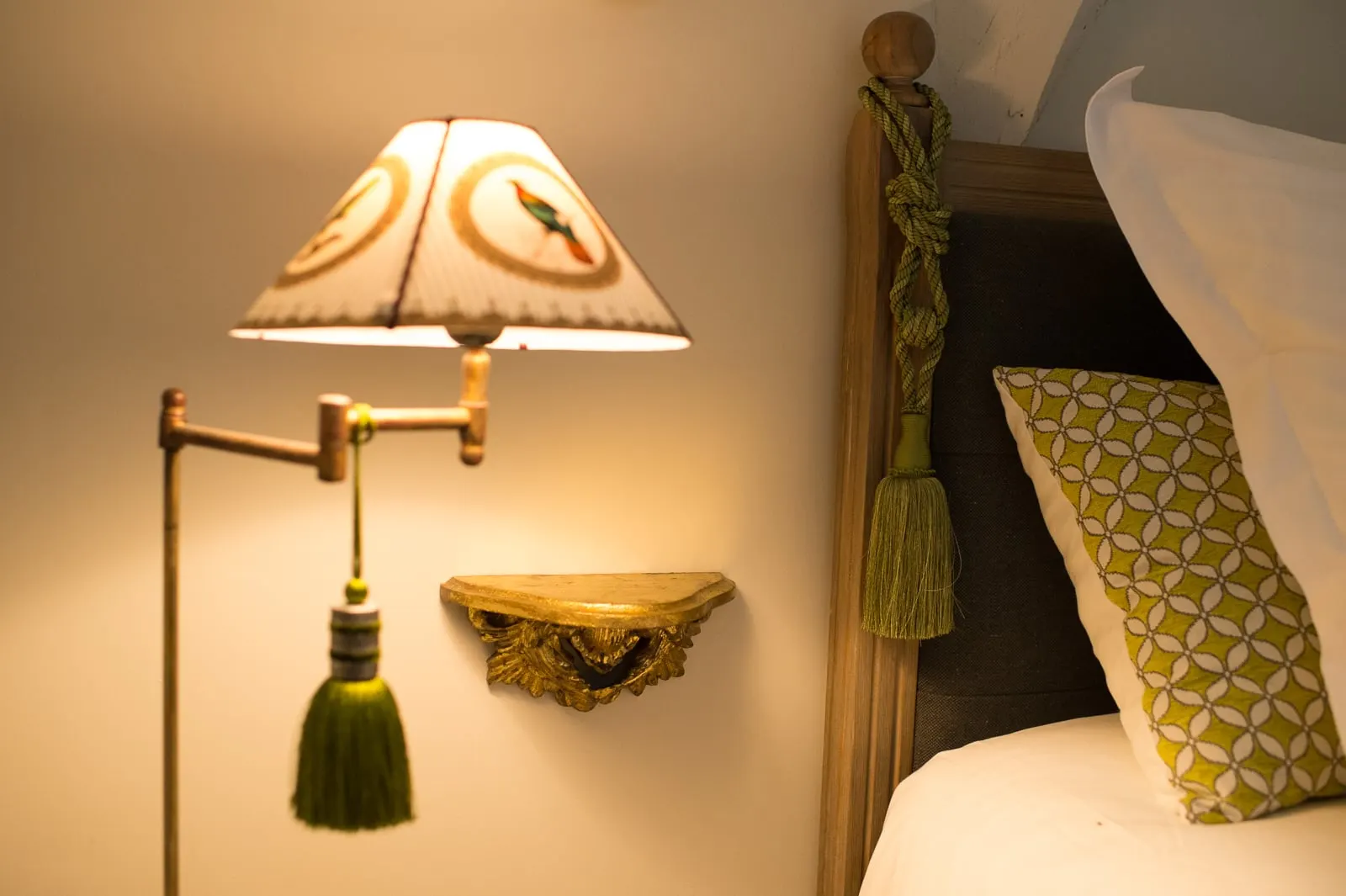 Reading lamp with a bird-patterned shade, green tassel and gilt shelf by the bed, La Folie Saint Julien