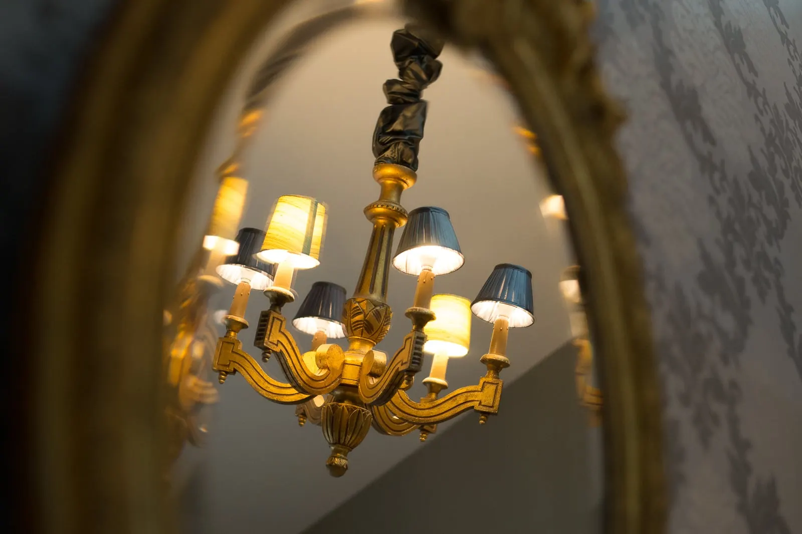 Gilded chandelier with grey and yellow shades reflected in an oval mirror, La Folie Saint Julien