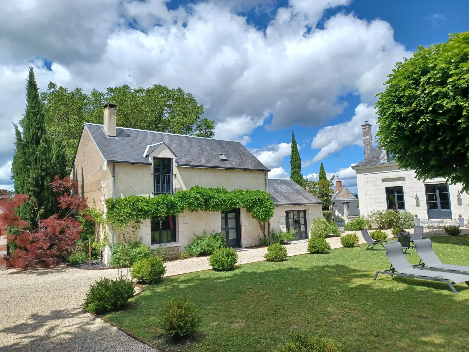 Stone house covered in wisteria, lawn and loungers under a cloudy sky, La Folie Saint Julien