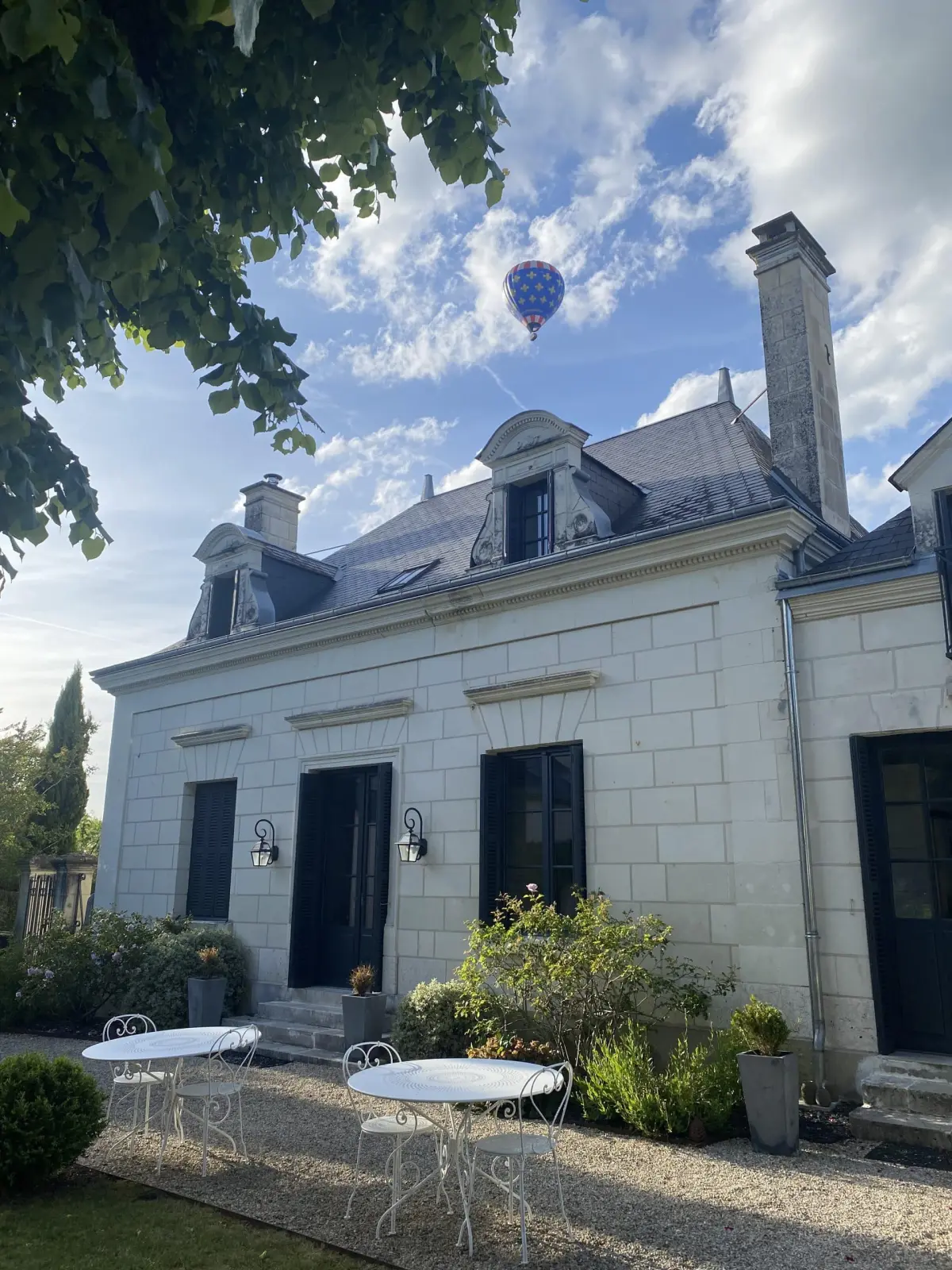 Hot-air balloon above the tufa stone house with dormer windows and its white tables, La Folie Saint Julien