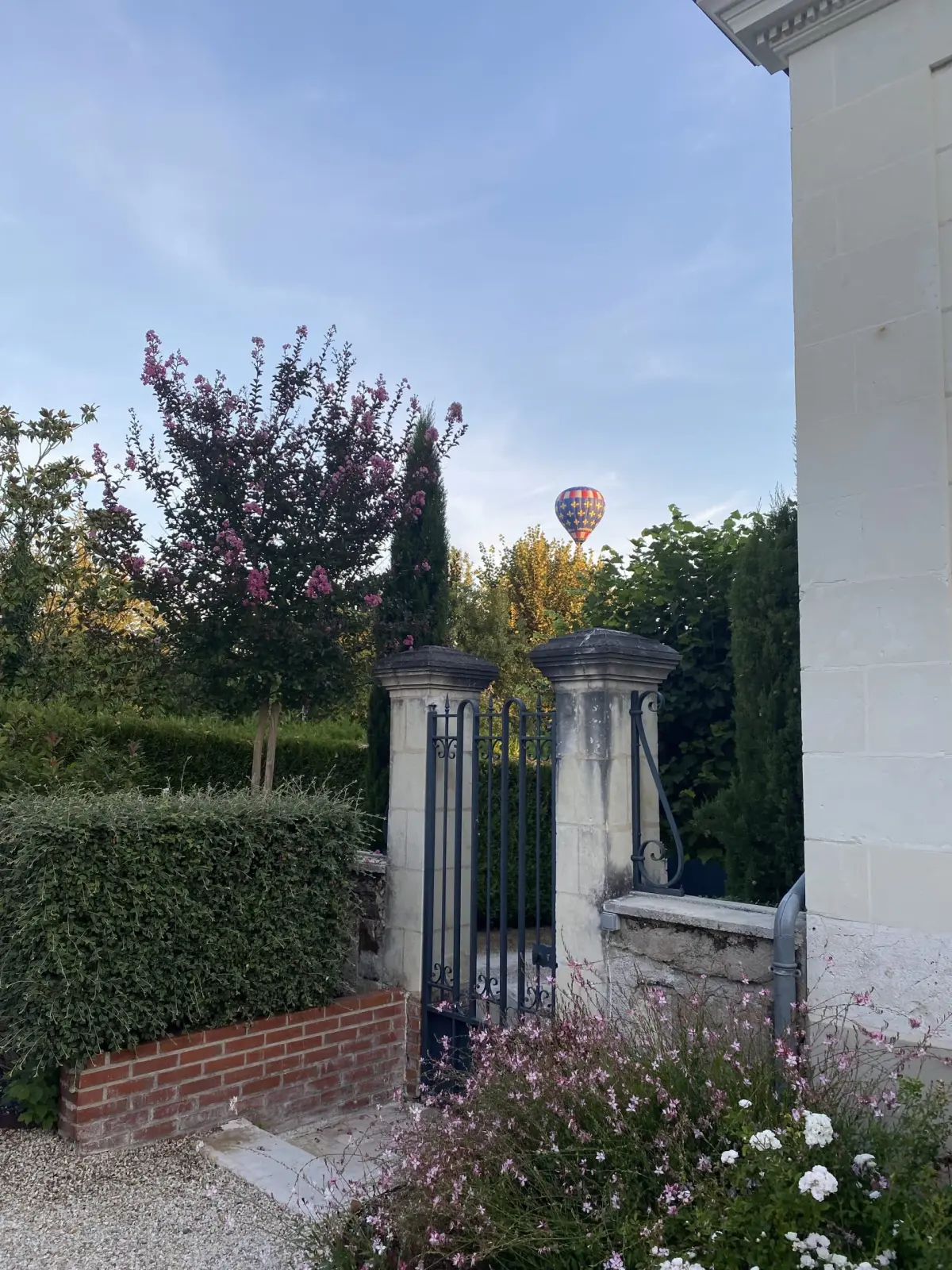 Hot-air balloon in the sky above a wrought-iron gate and a flowering hedge, La Folie Saint Julien