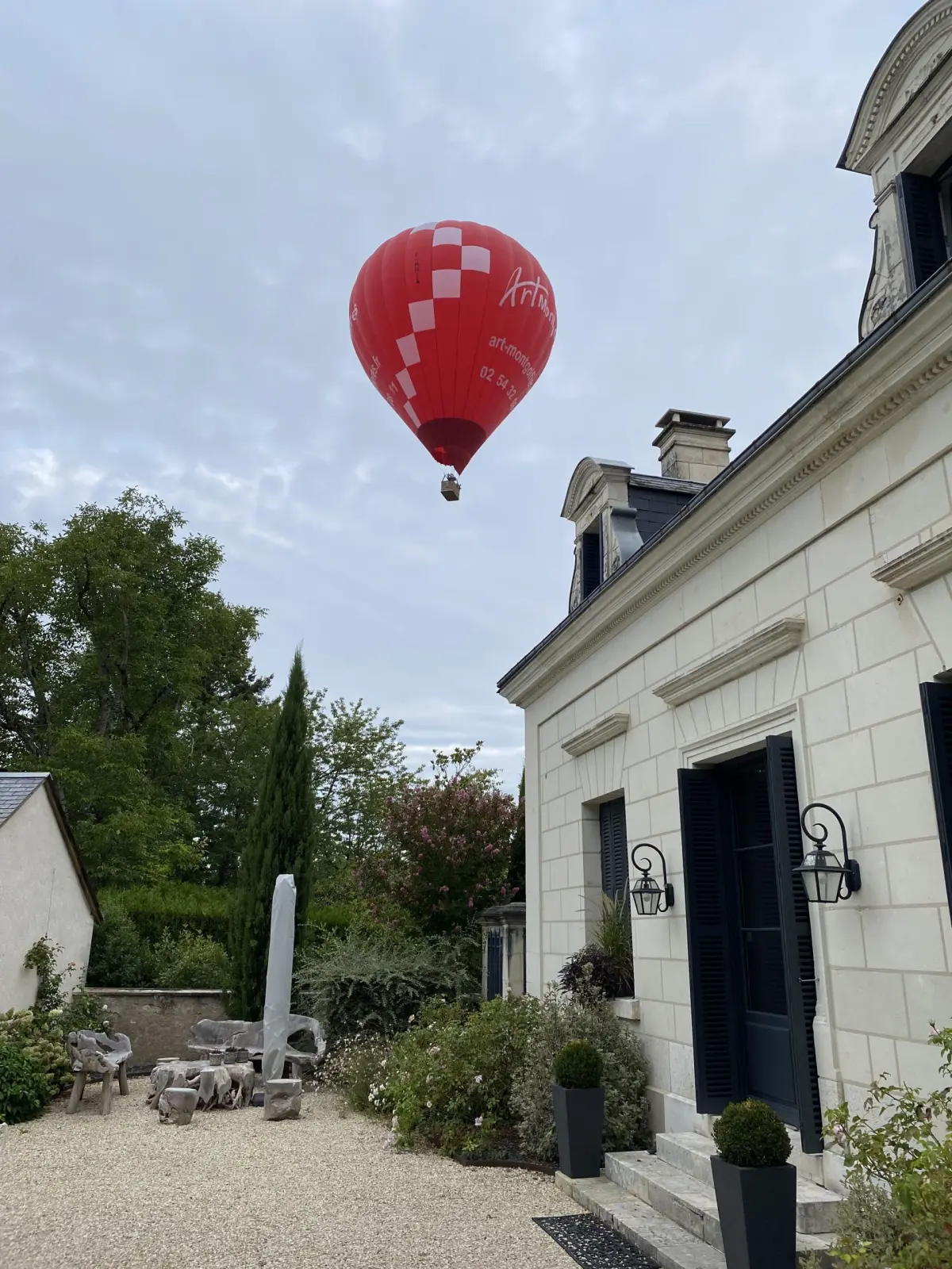 Low-flying red and white hot-air balloon above the courtyard and facade, La Folie Saint Julien