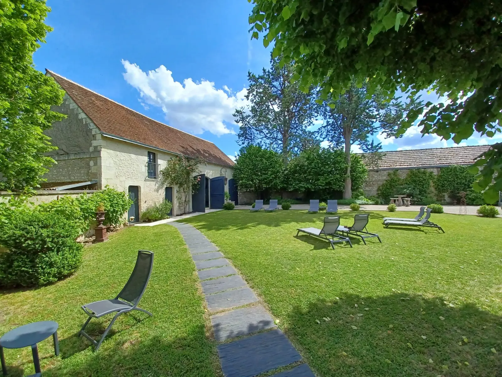Lawn with loungers and a paved path leading to the stone outbuildings, La Folie Saint Julien