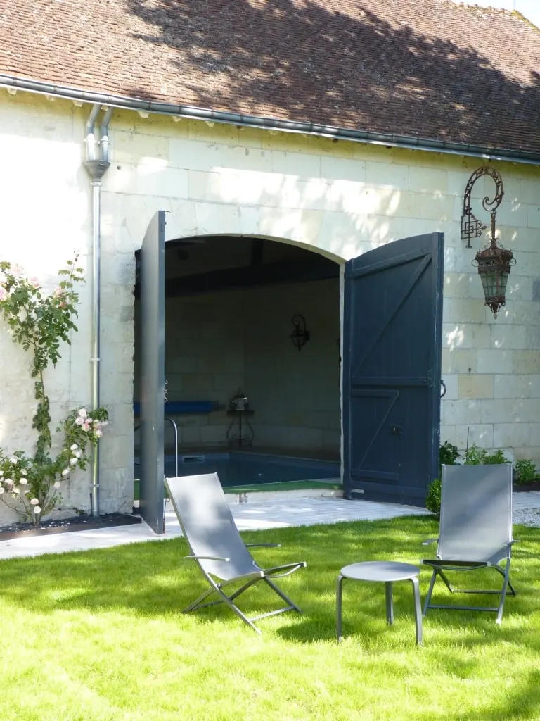 Stone outbuilding with doors open onto the indoor pool, loungers on the lawn, La Folie Saint Julien