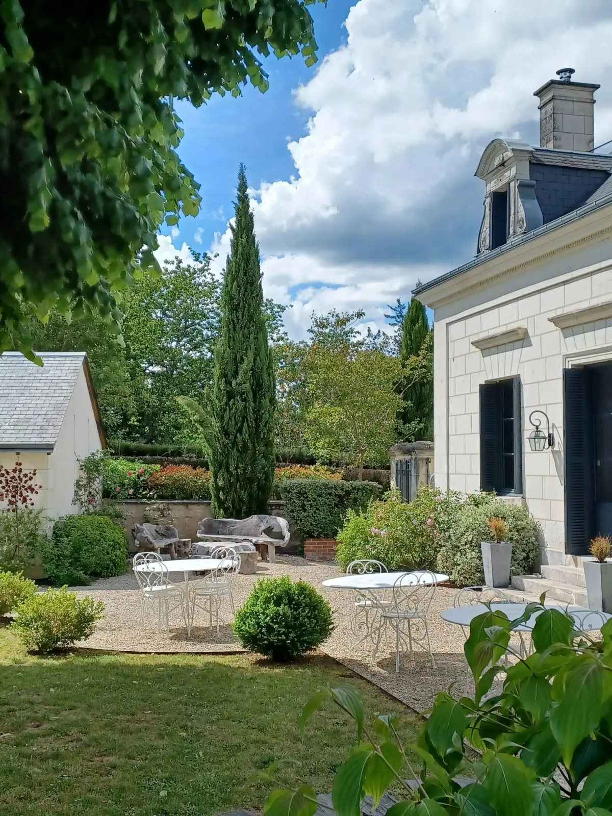 Gravel terrace with white wrought-iron tables at the foot of the tufa stone house, La Folie Saint Julien