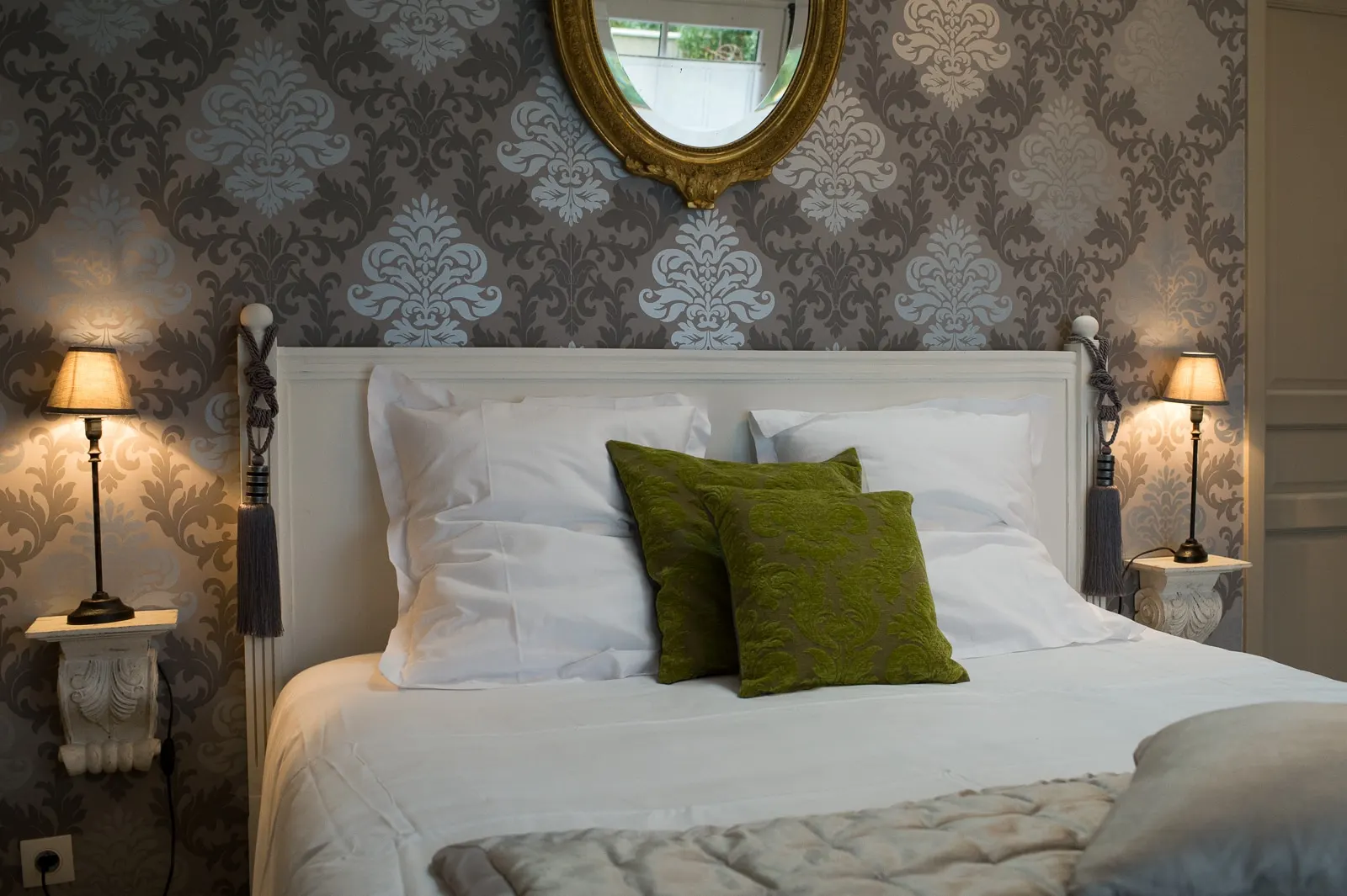 White headboard, green cushions and bedside lamps against damask wallpaper, La Folie Saint Julien