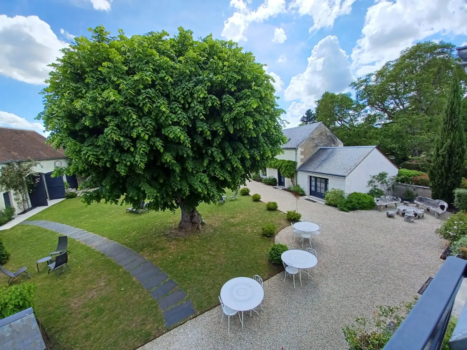 Bird's-eye view of the gravel courtyard, its white tables, the large tree and the lawn, La Folie Saint Julien