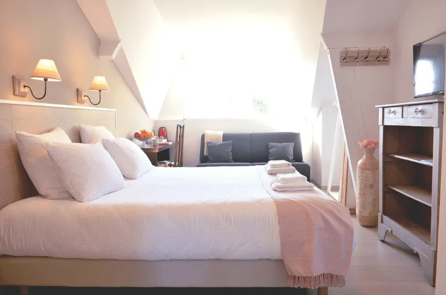 Attic bedroom at Villa Glen Tara with double bed, folded towels, grey sofa and chest of drawers