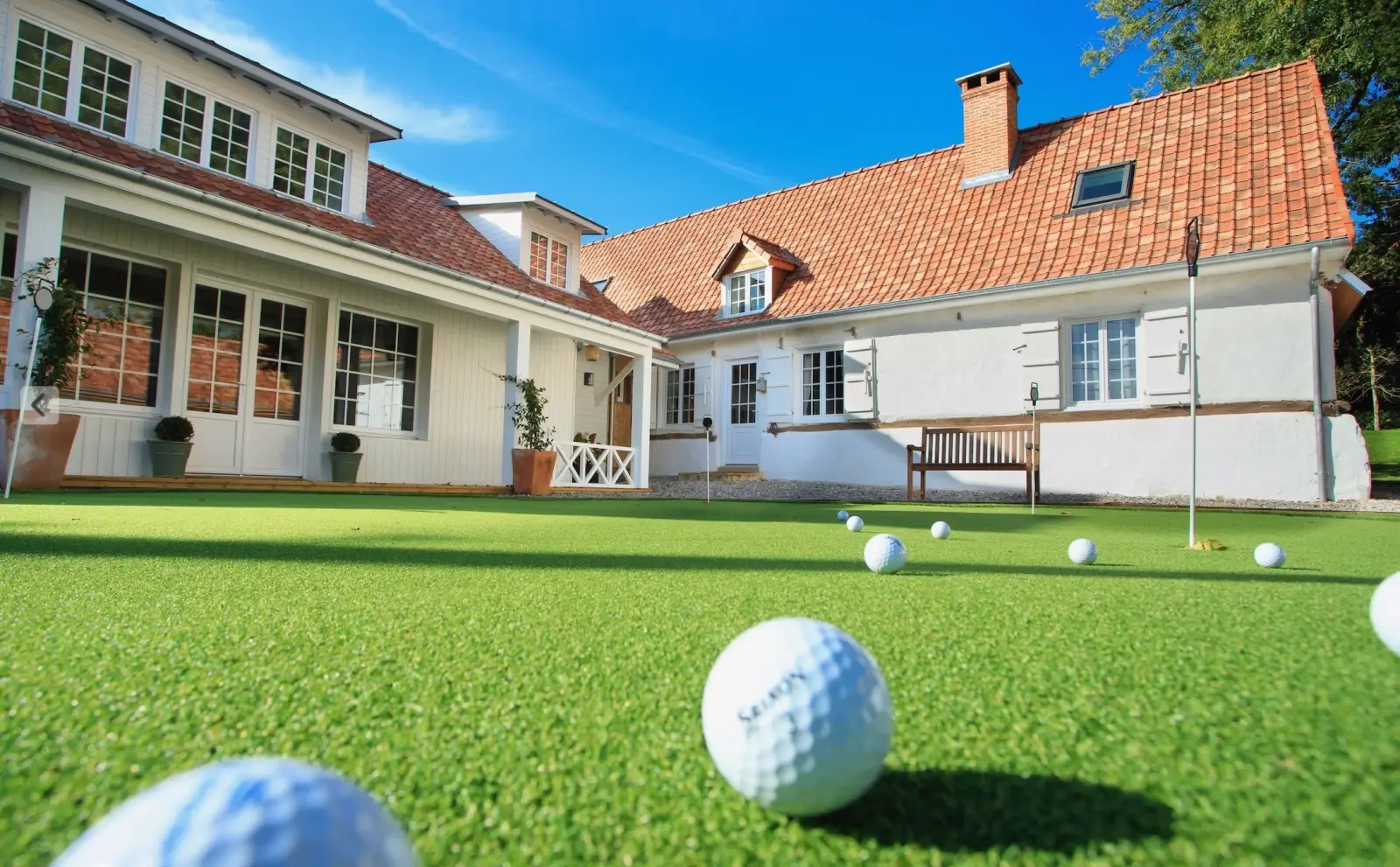 Green de putting avec balles de golf devant une maison blanche au toit de tuiles orangées