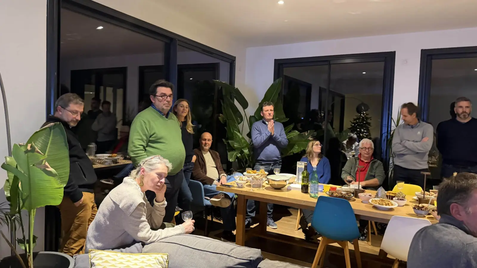 Group of hosts chatting in a living room around a large laden table, with glass doors behind