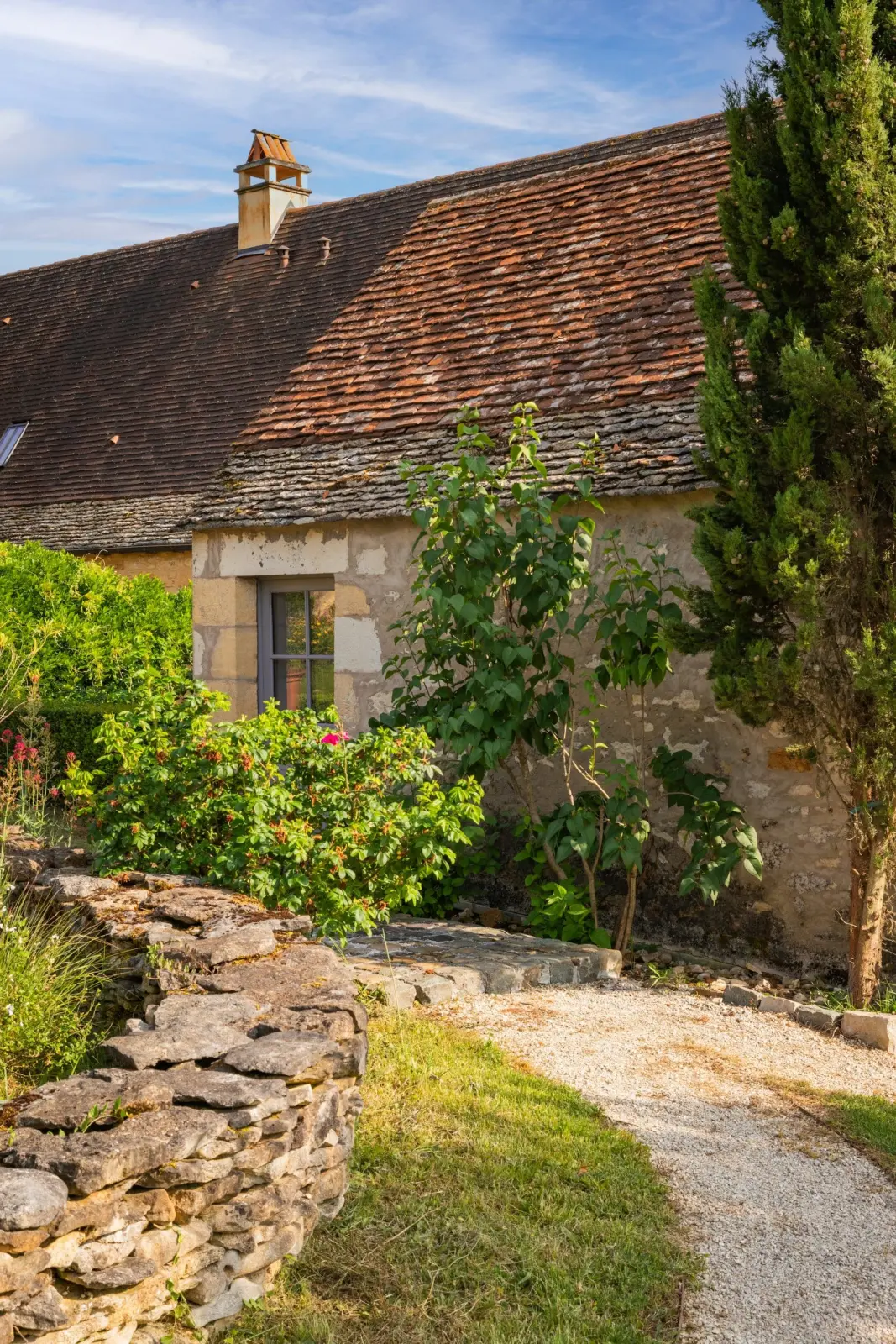 Entrance to the gîte at Les Hauts de Saint-Vincent: stone house with tiled roof, low wall and gravel path