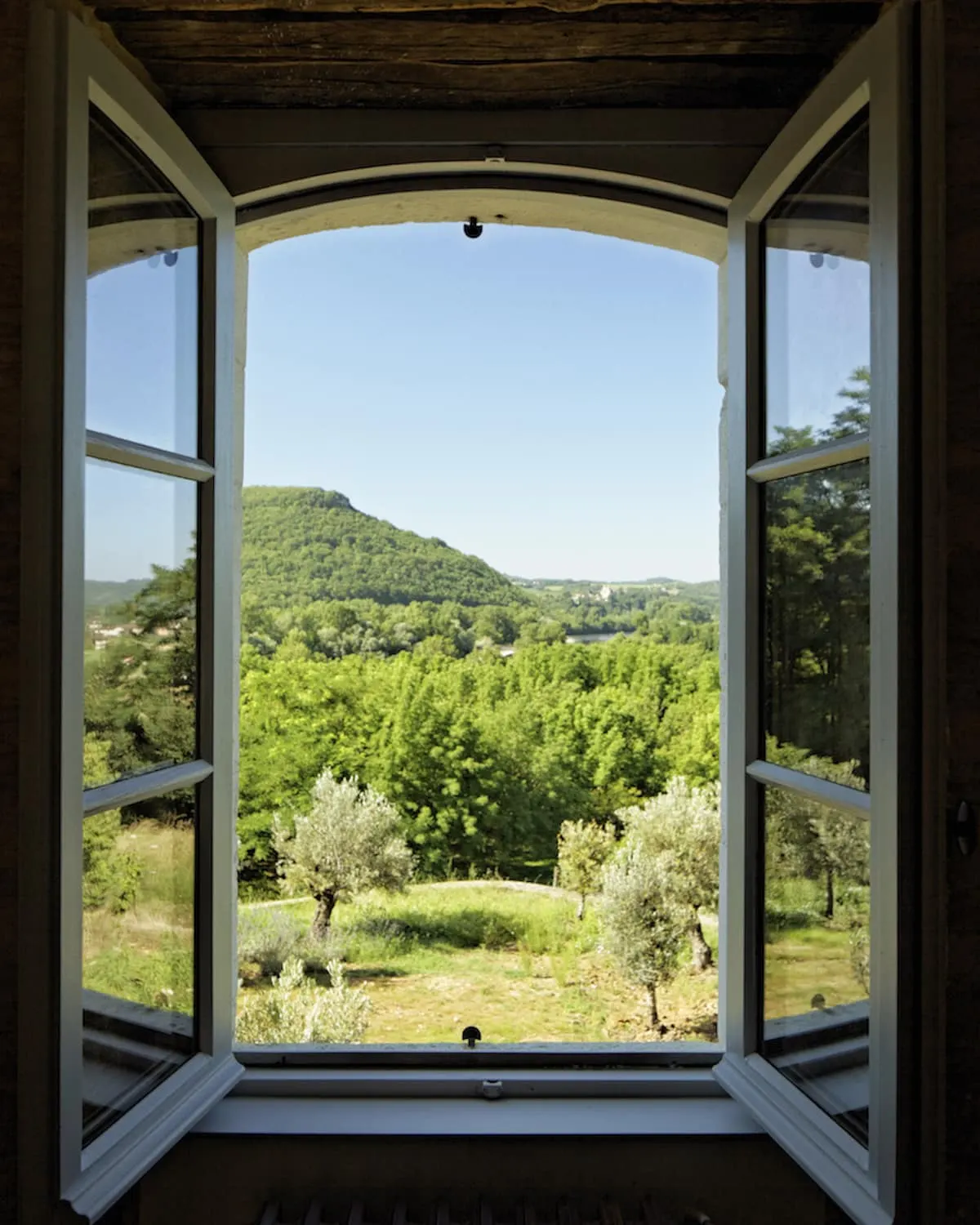 Open bedroom window at Les Hauts de Saint-Vincent overlooking a wooded valley, olive trees and a hill