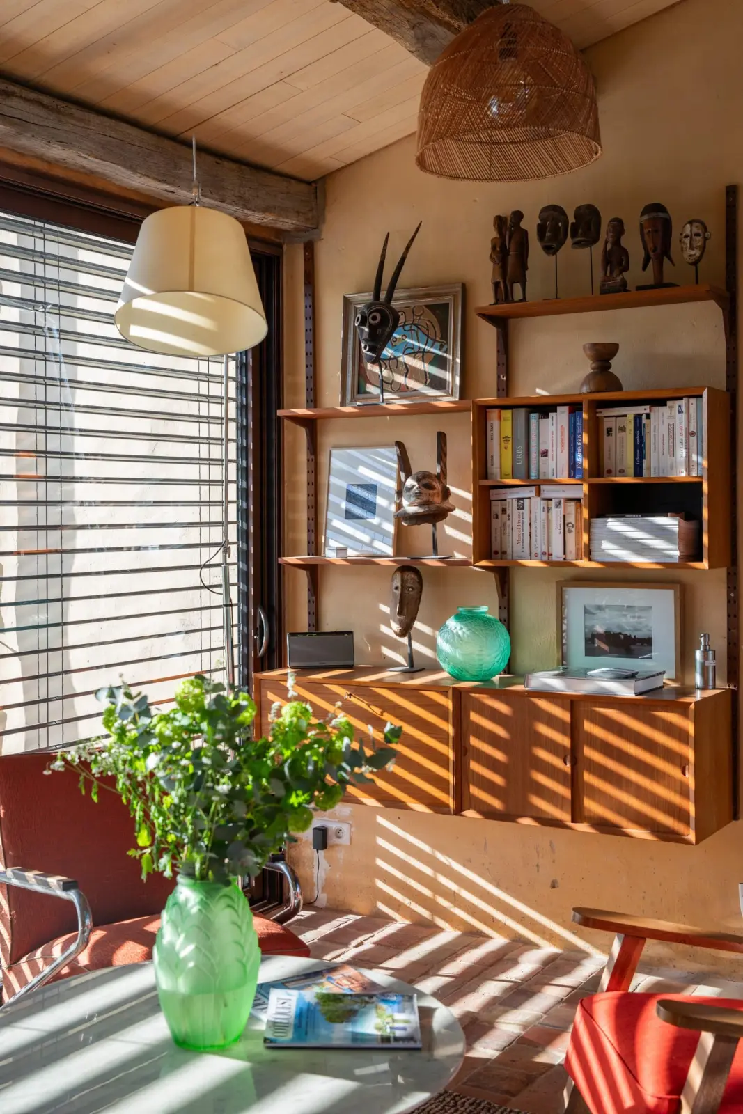 Reading corner at Les Hauts de Saint-Vincent: bookshelves, African masks, red armchairs and sunlight