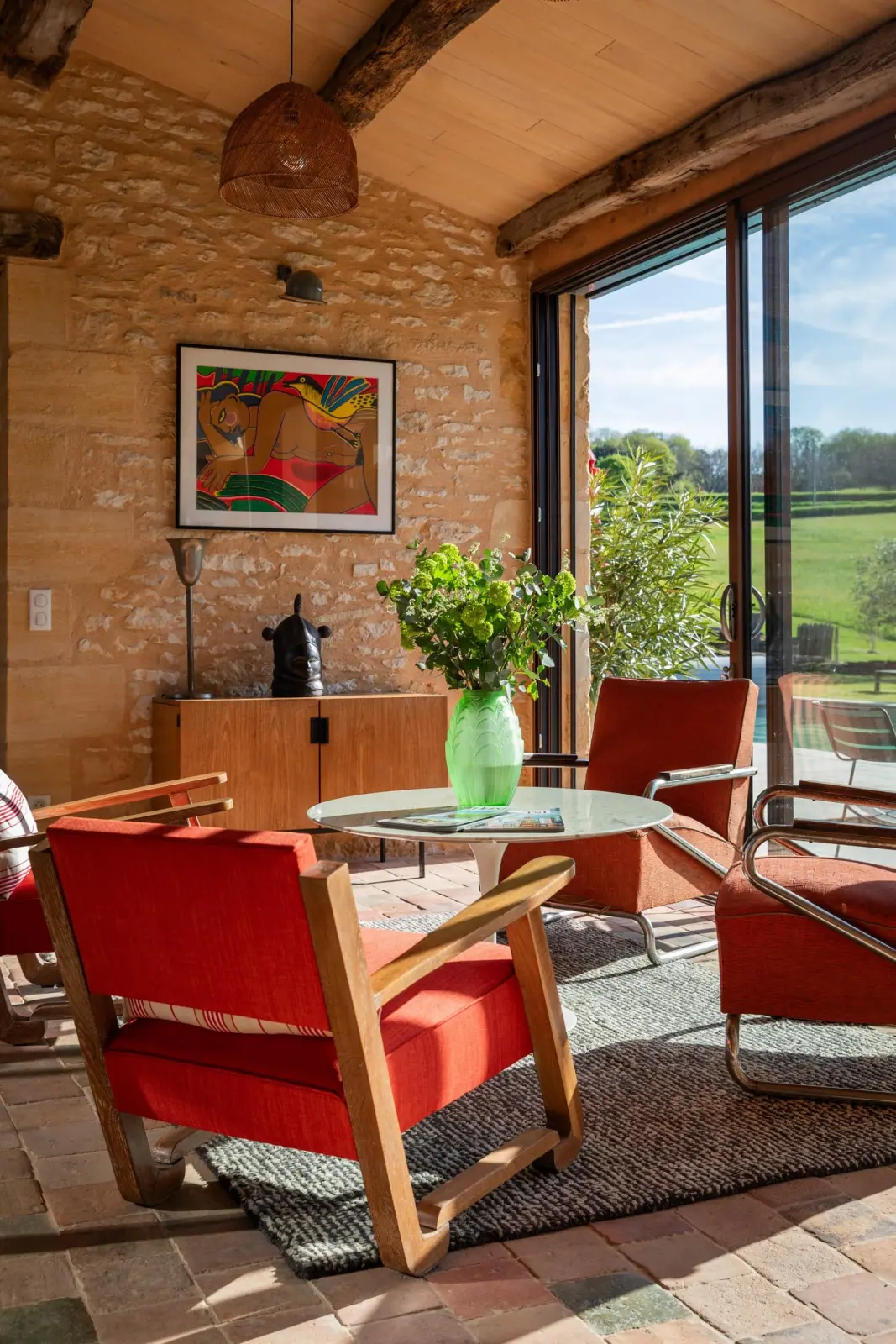 Gallery at Les Hauts de Saint-Vincent: red armchairs, glass table, stone walls and glass doors onto the garden