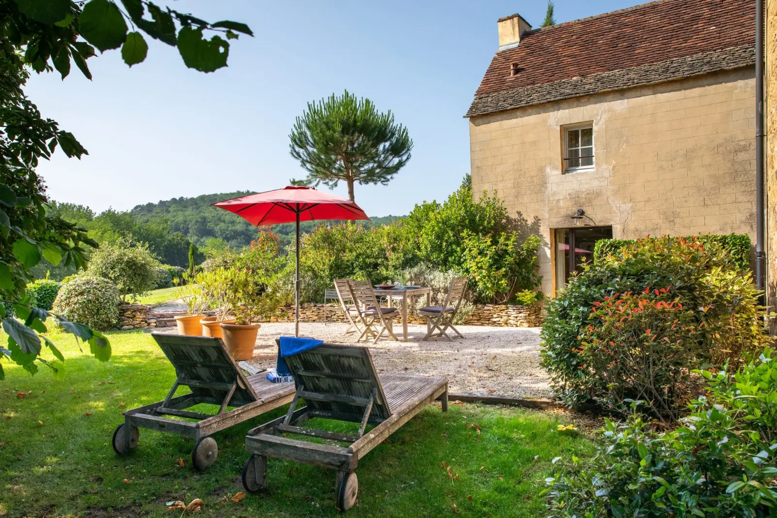 Stone gîte at Les Hauts de Saint-Vincent with a gravel terrace, red parasol, table and sun loungers