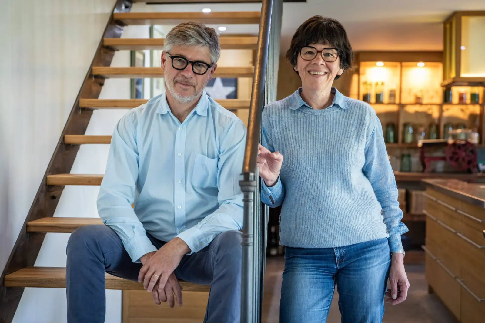 The hosts of Les Hauts de Saint-Vincent, smiling at the foot of a wooden staircase