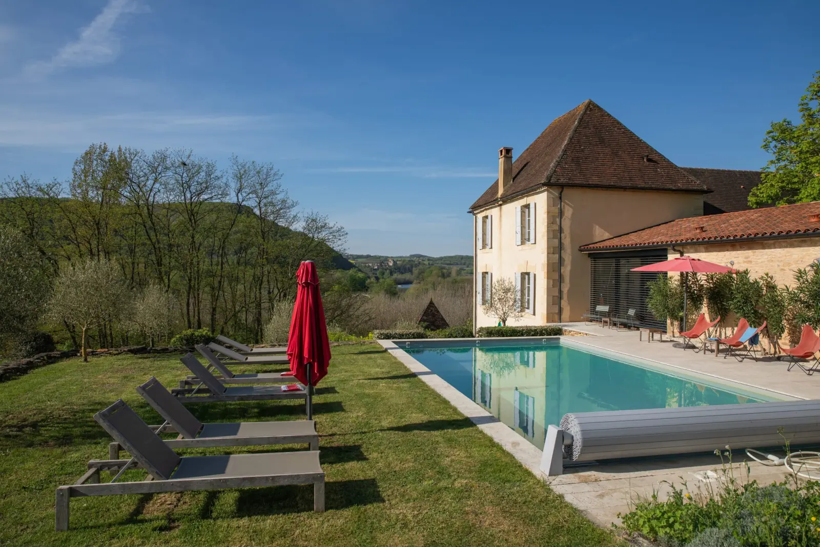 Piscine des Hauts de Saint-Vincent, transats et parasol rouge face à la vallée, maison en pierre