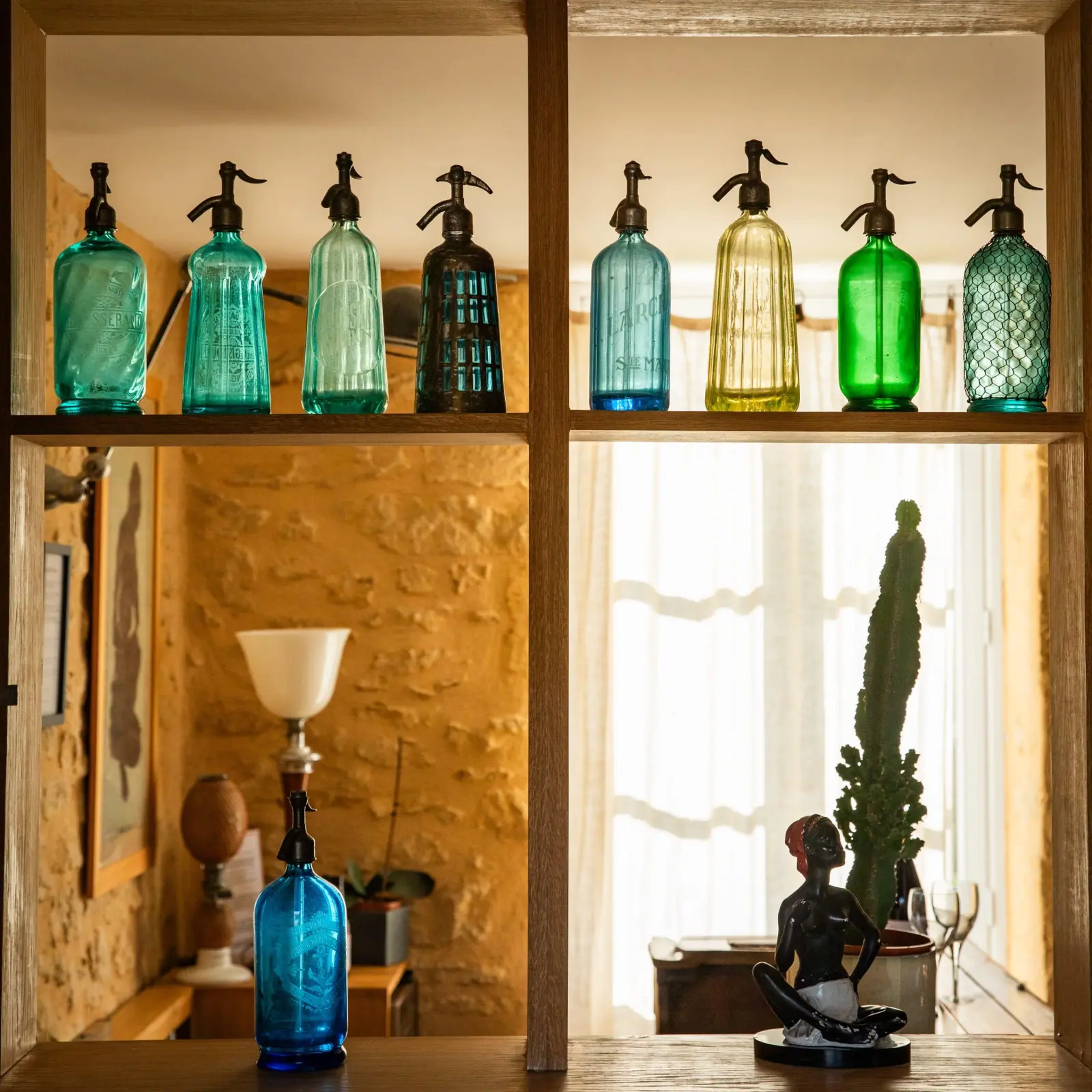Old coloured glass soda siphons lined up on a wooden shelf in front of a stone wall, Les Hauts de Saint-Vincent