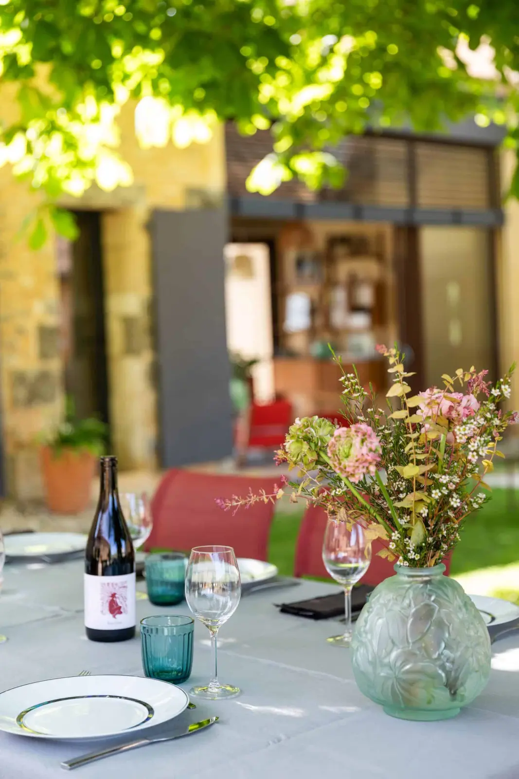 Table d'hôtes laid in the garden at Les Hauts de Saint-Vincent, with a vase of wild flowers, glasses and wine