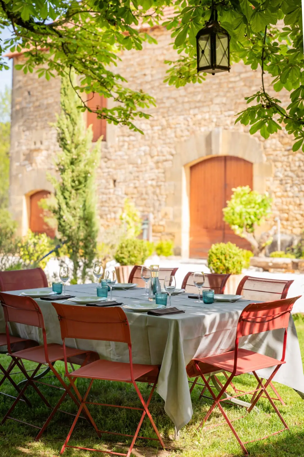 Table d'hôtes and orange chairs in the garden at Les Hauts de Saint-Vincent, in front of a stone building