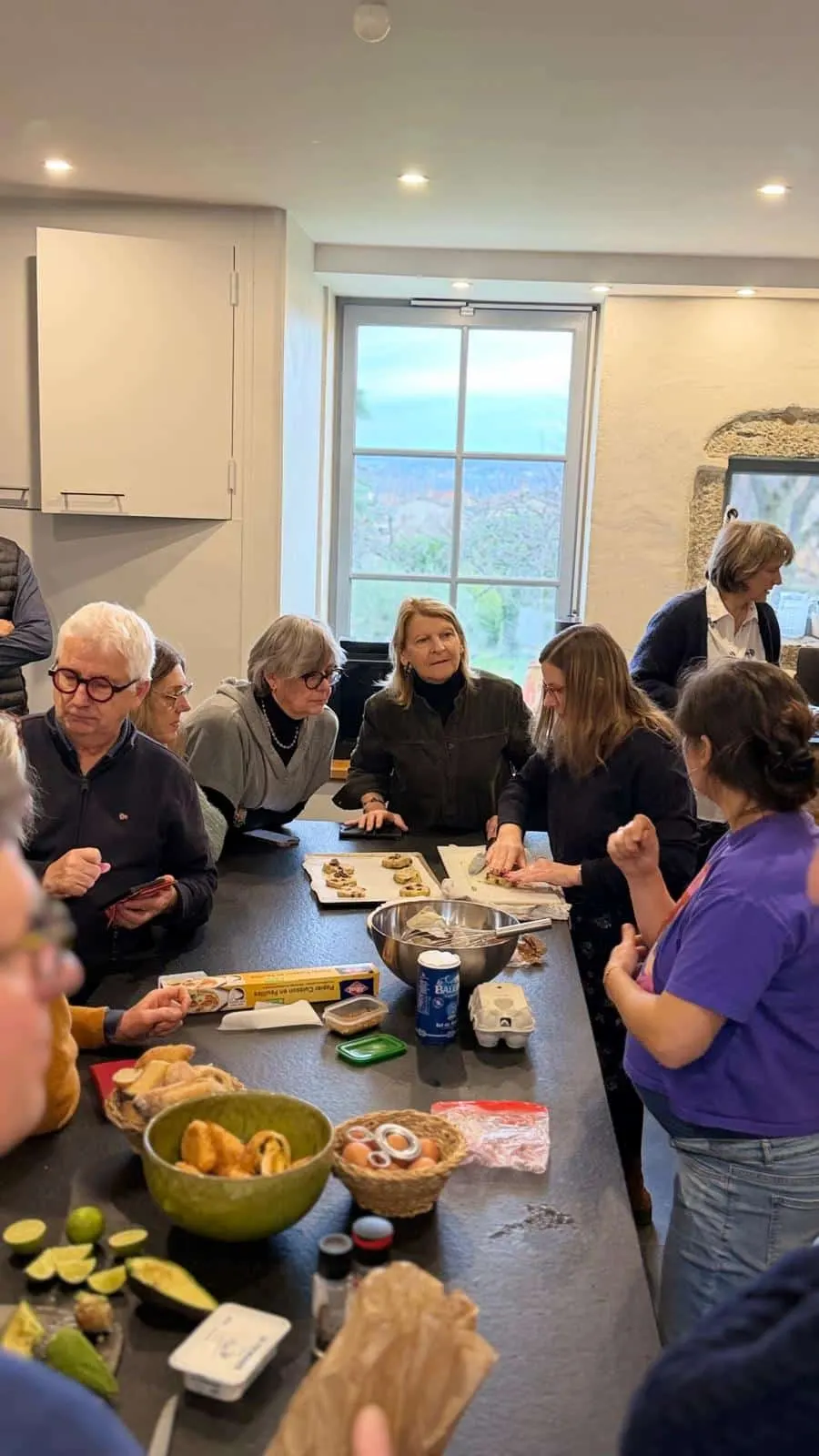 Hosts sharing a meal around a table in a bright kitchen, bread and fruit on the worktop