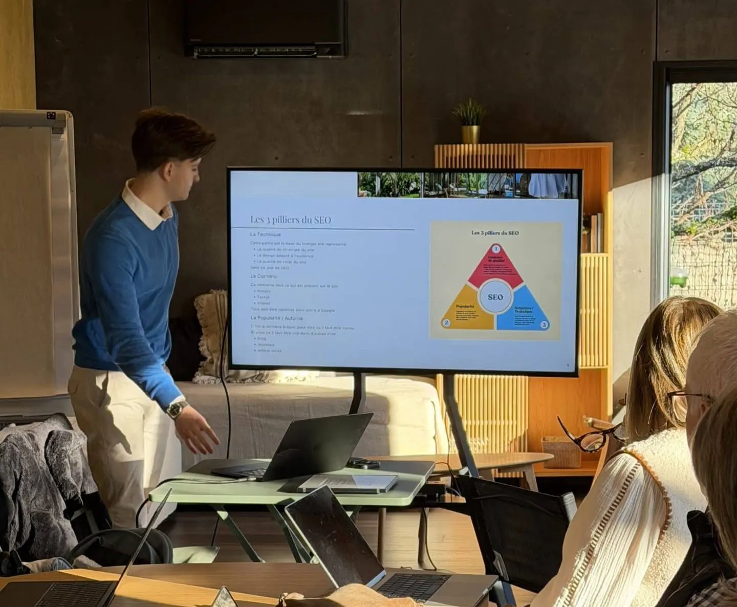 Speaker presenting slides on a large screen during a meeting, with attendees listening