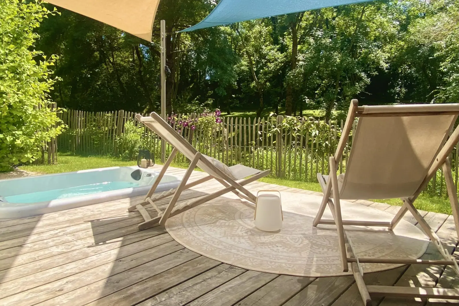 Wooden deck at Kassiopée with deckchairs, shade sails and a hot tub, facing the garden and trees