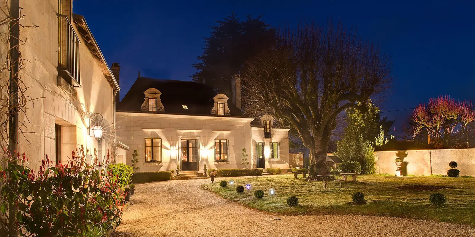 La Folie Saint-Julien illuminée de nuit, avec sa cour gravillonnée, ses buis taillés et son grand platane