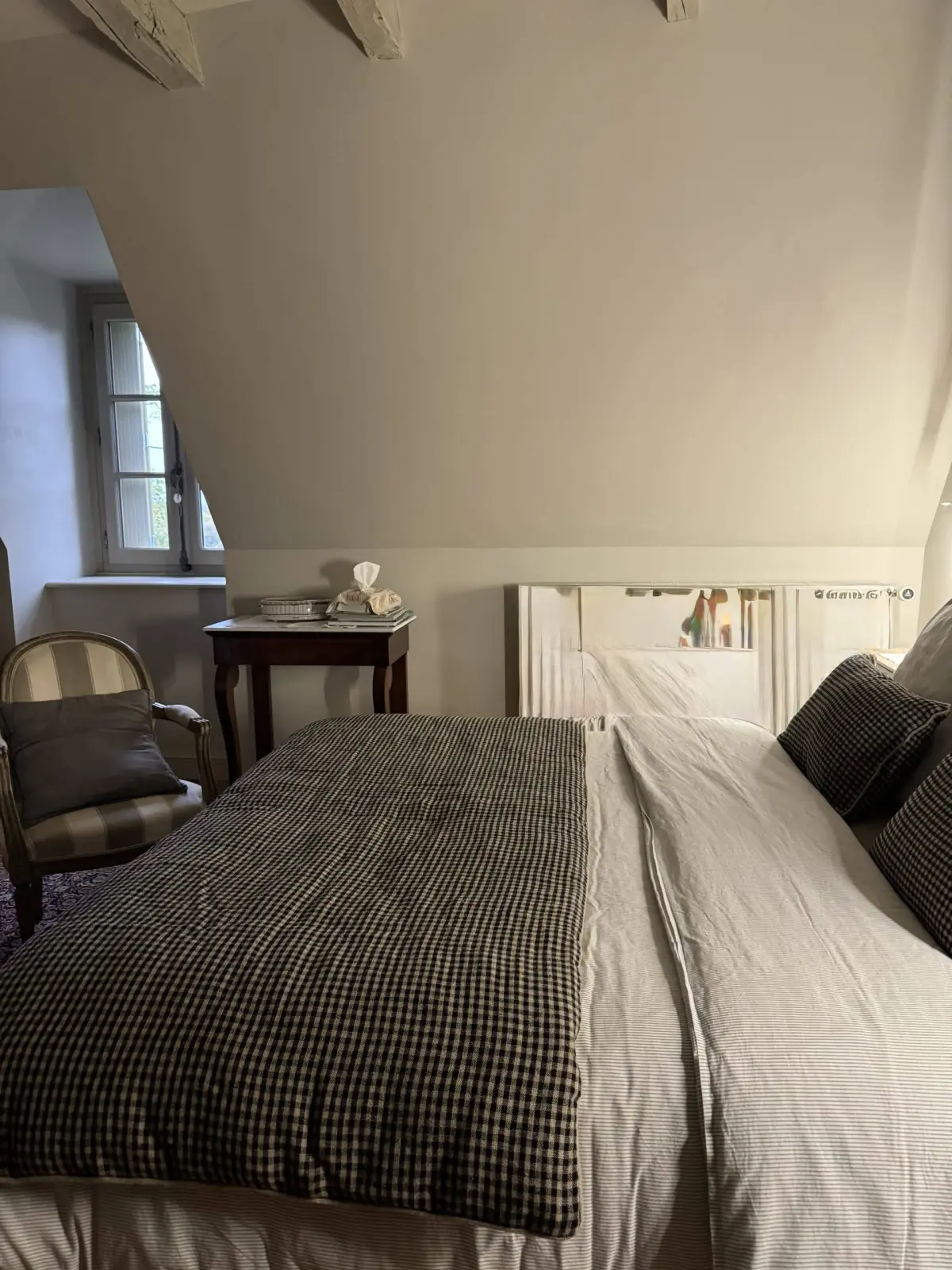 An attic bedroom at La Fournio: double bed with a gingham throw, striped armchair and small table