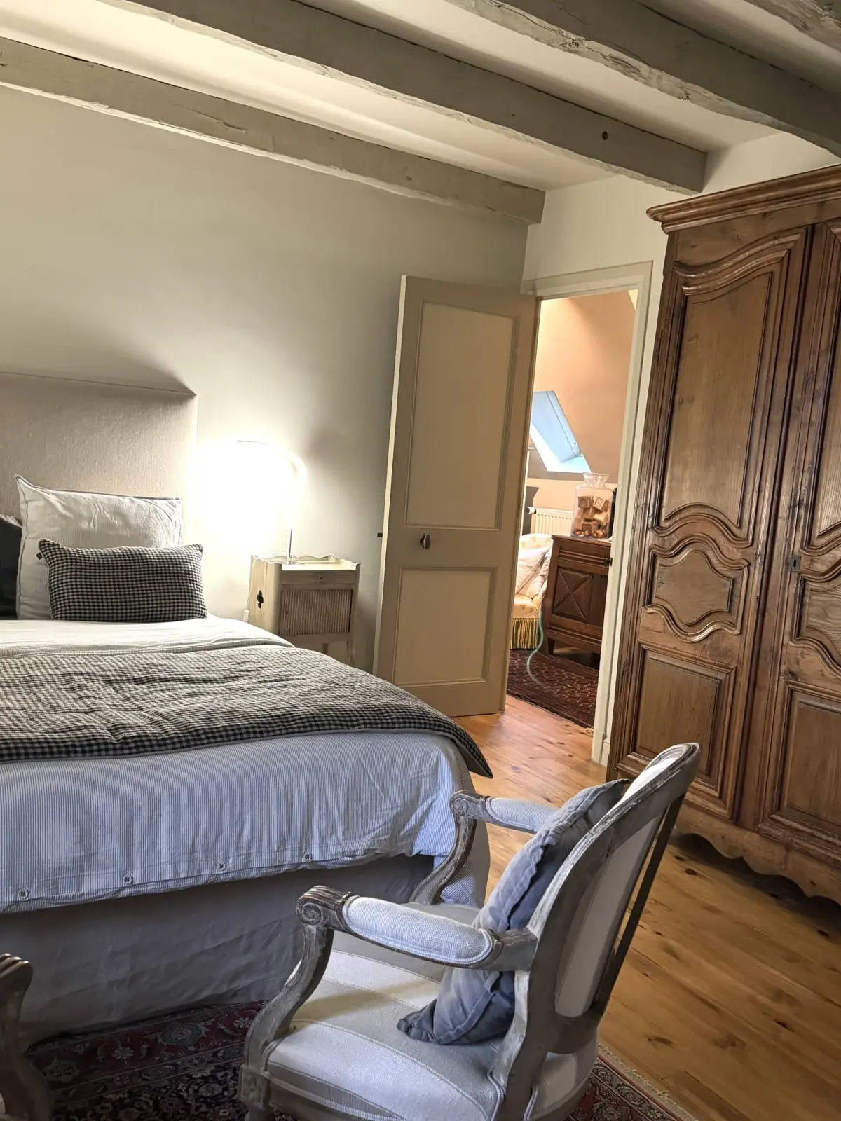 A bedroom at La Fournio: pale beams, double bed, large wooden wardrobe and an antique armchair