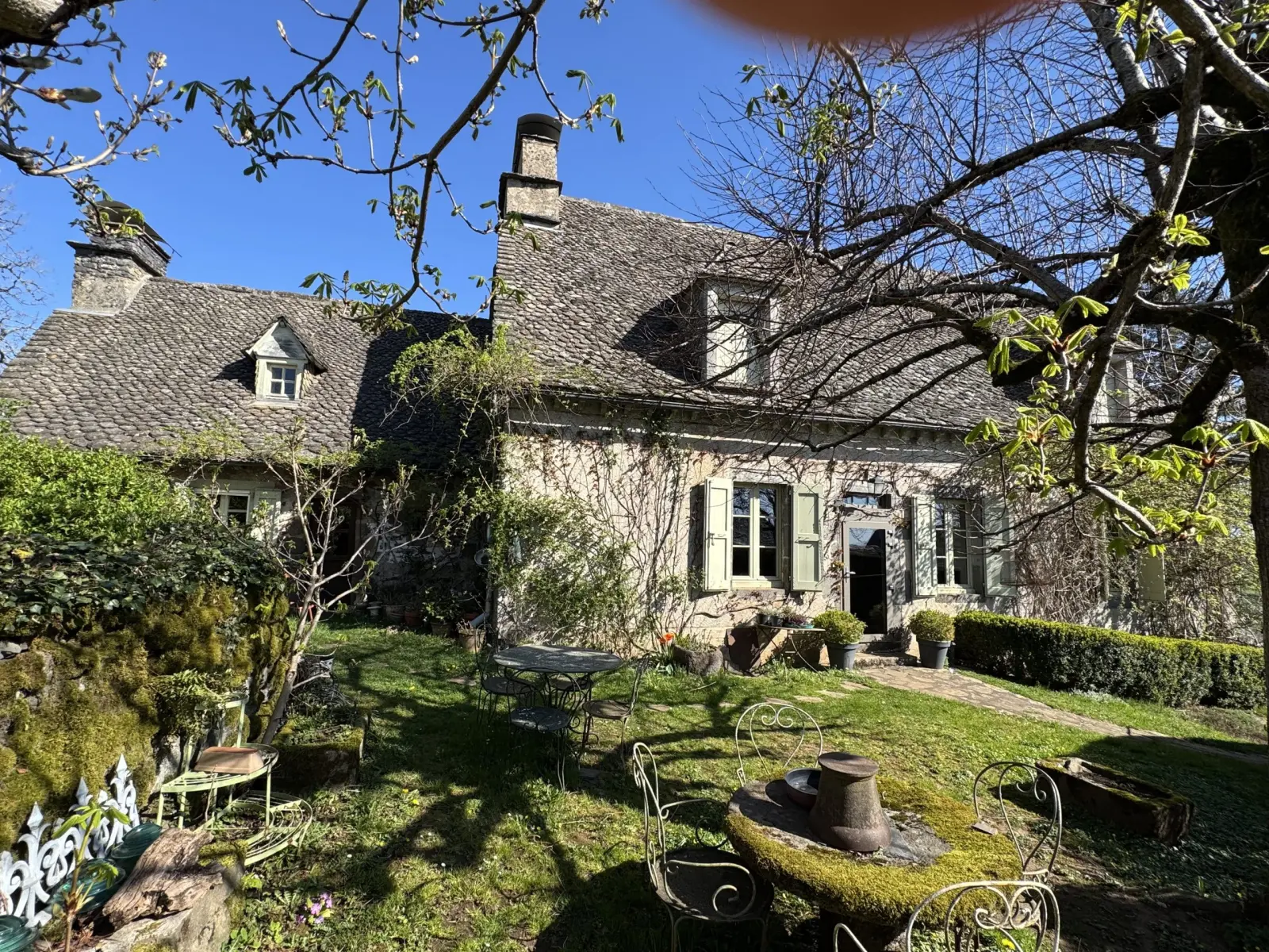 Stone house with a stone-slab roof, green shutters and a garden with wrought-iron tables, La Fournio