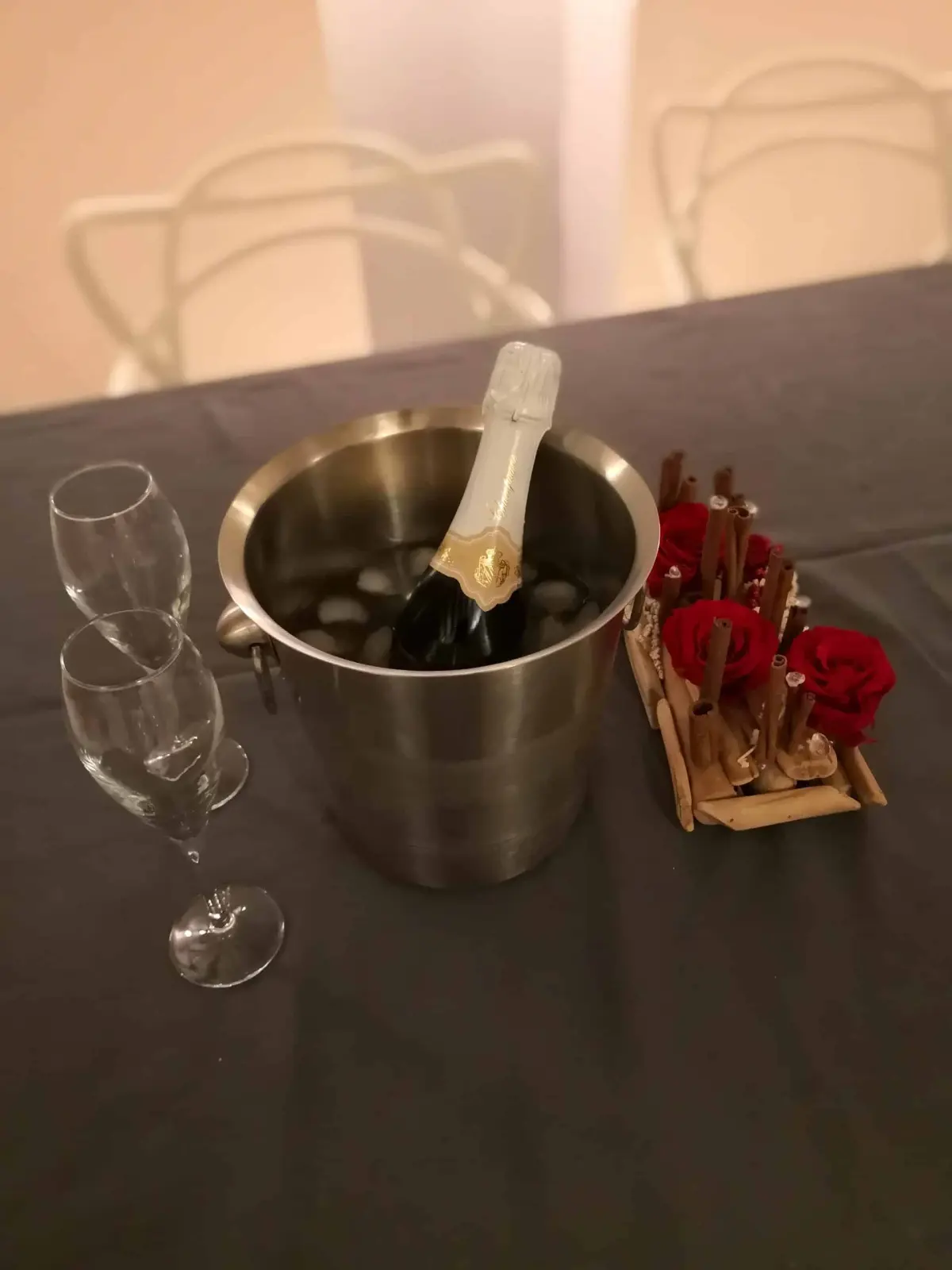 Bottle of champagne in an ice bucket, two flutes and a red rose centrepiece on a grey tablecloth, La Vie Voyage