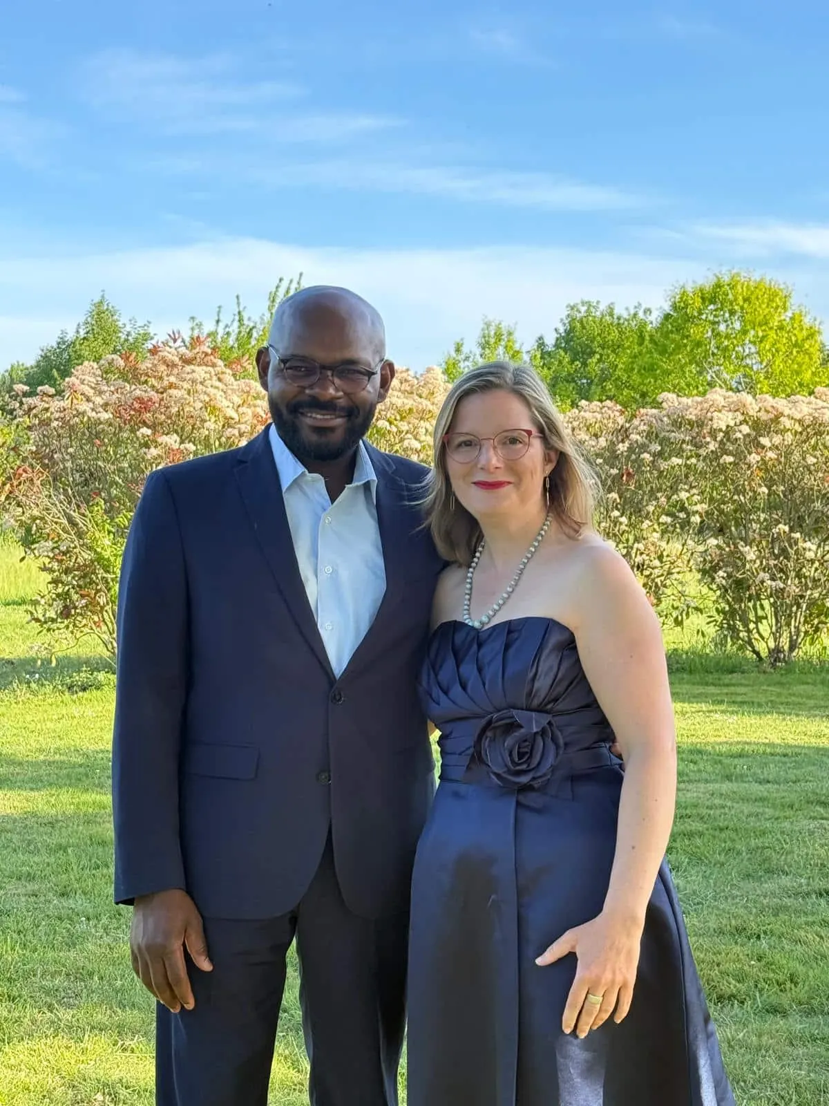 The hosts of La Vie Voyage in evening wear posing in a flowering garden under a blue sky