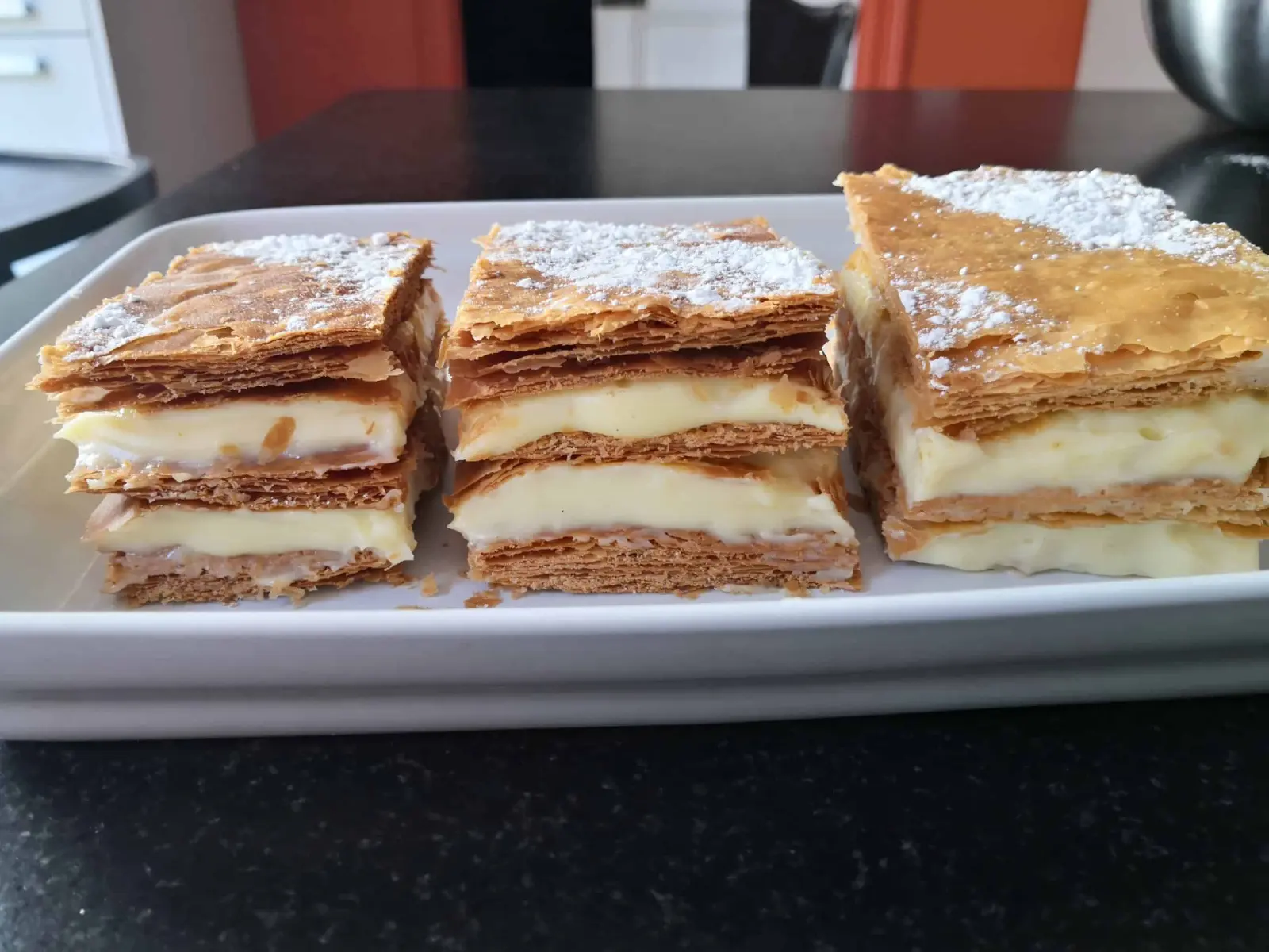 Three slices of cream mille-feuille dusted with icing sugar on a white dish at La Vie Voyage