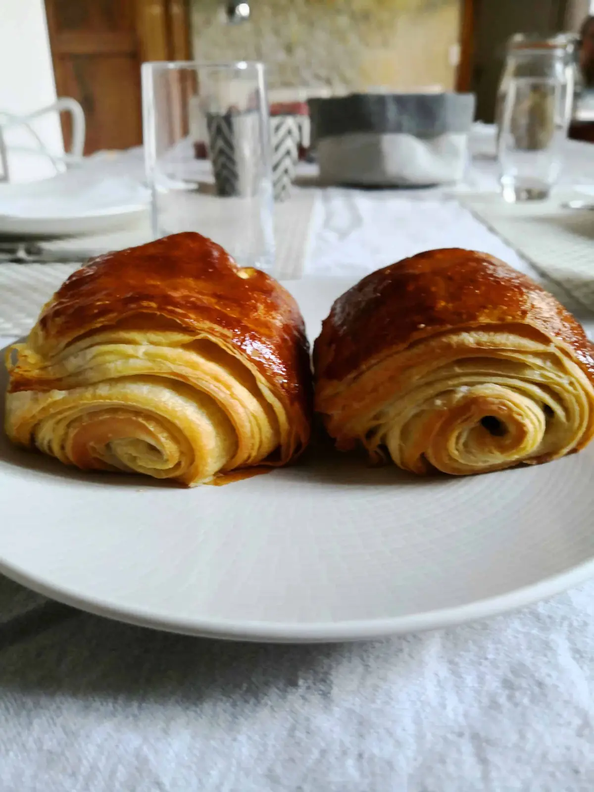 Two flaky, golden pains au chocolat on a white plate at the breakfast table of La Vie Voyage