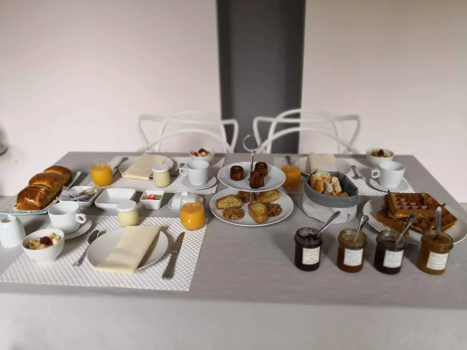 Breakfast table with brioches, waffles, cannelés, orange juice and jars of jam at La Vie Voyage