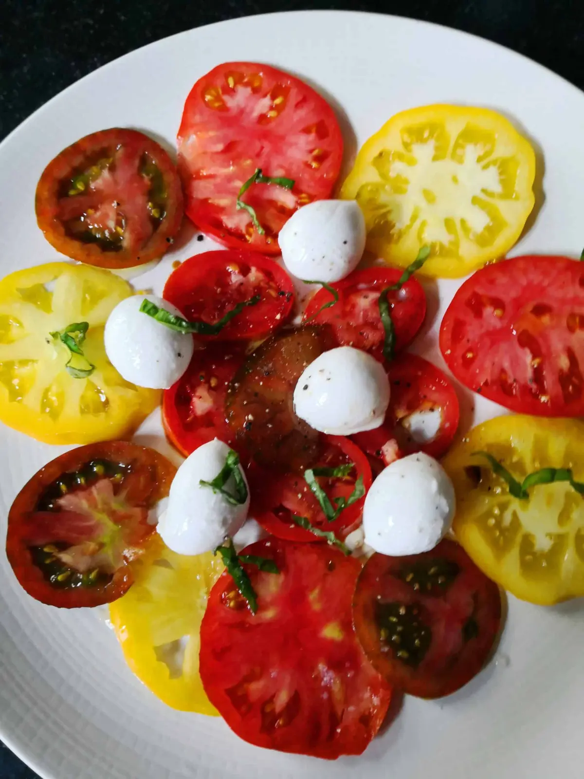 Plate of sliced red, yellow and dark tomatoes with mozzarella balls and basil at La Vie Voyage