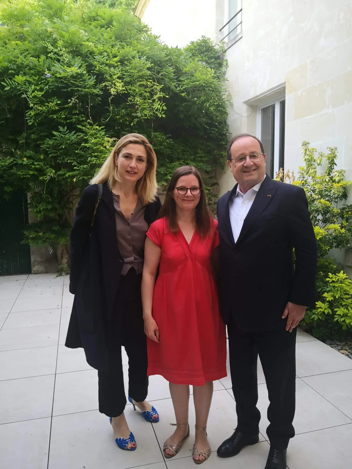 Three people posing together in a paved courtyard in front of a wisteria-covered wall at La Vie Voyage